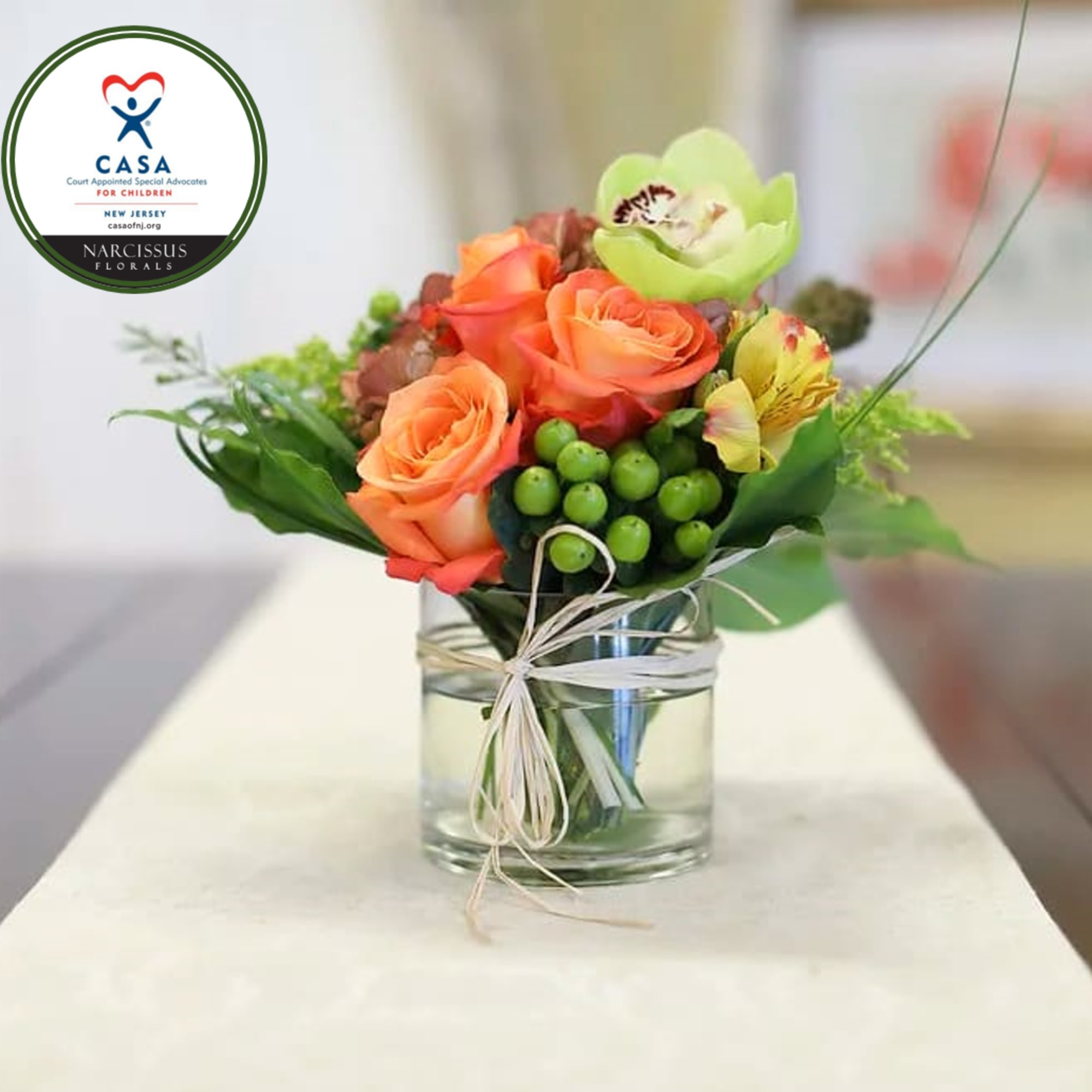 Orange roses and mixed blooms in a glass vase with a raffia tie