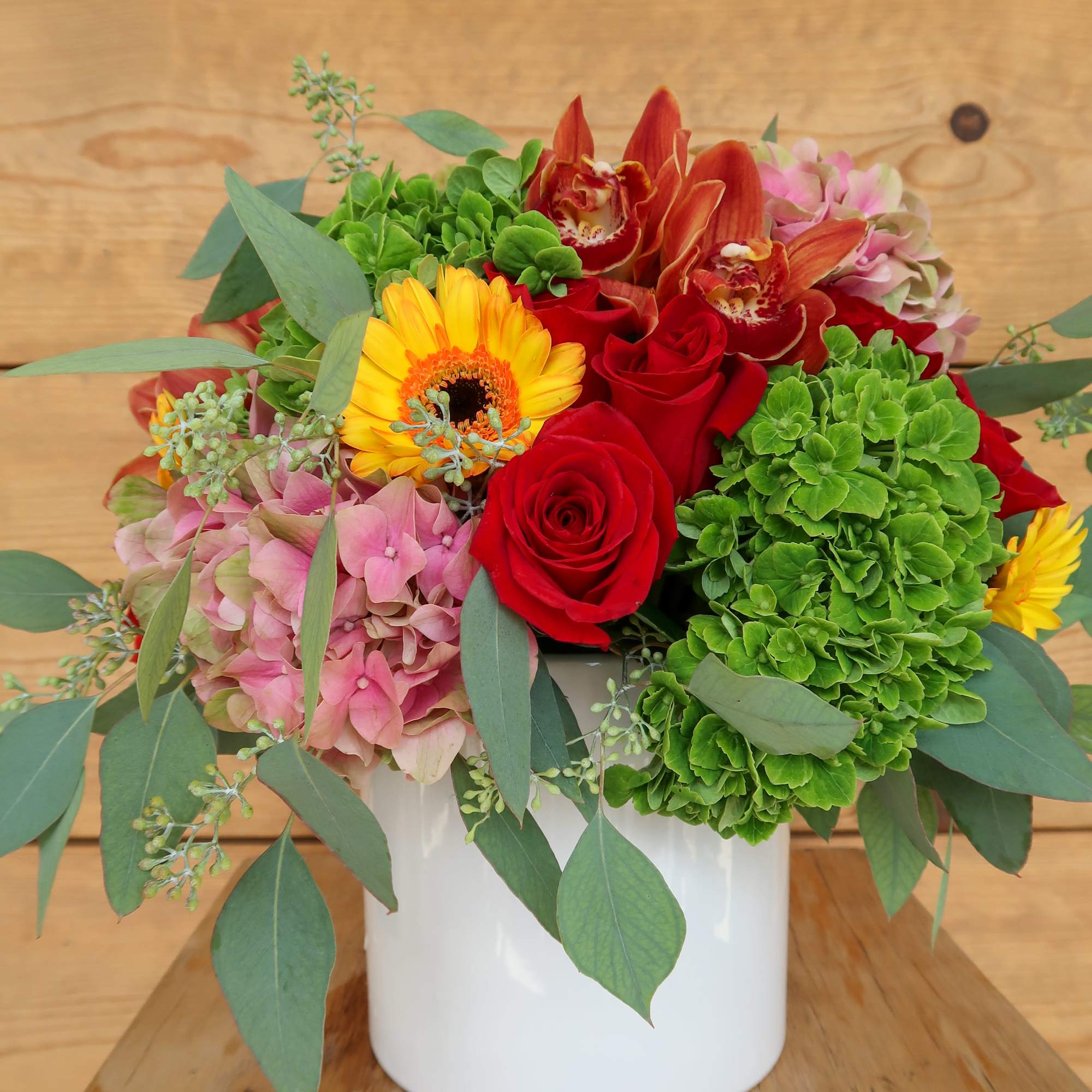Mixed bouquet of red roses, green hydrangeas, and orange orchids in a white vase