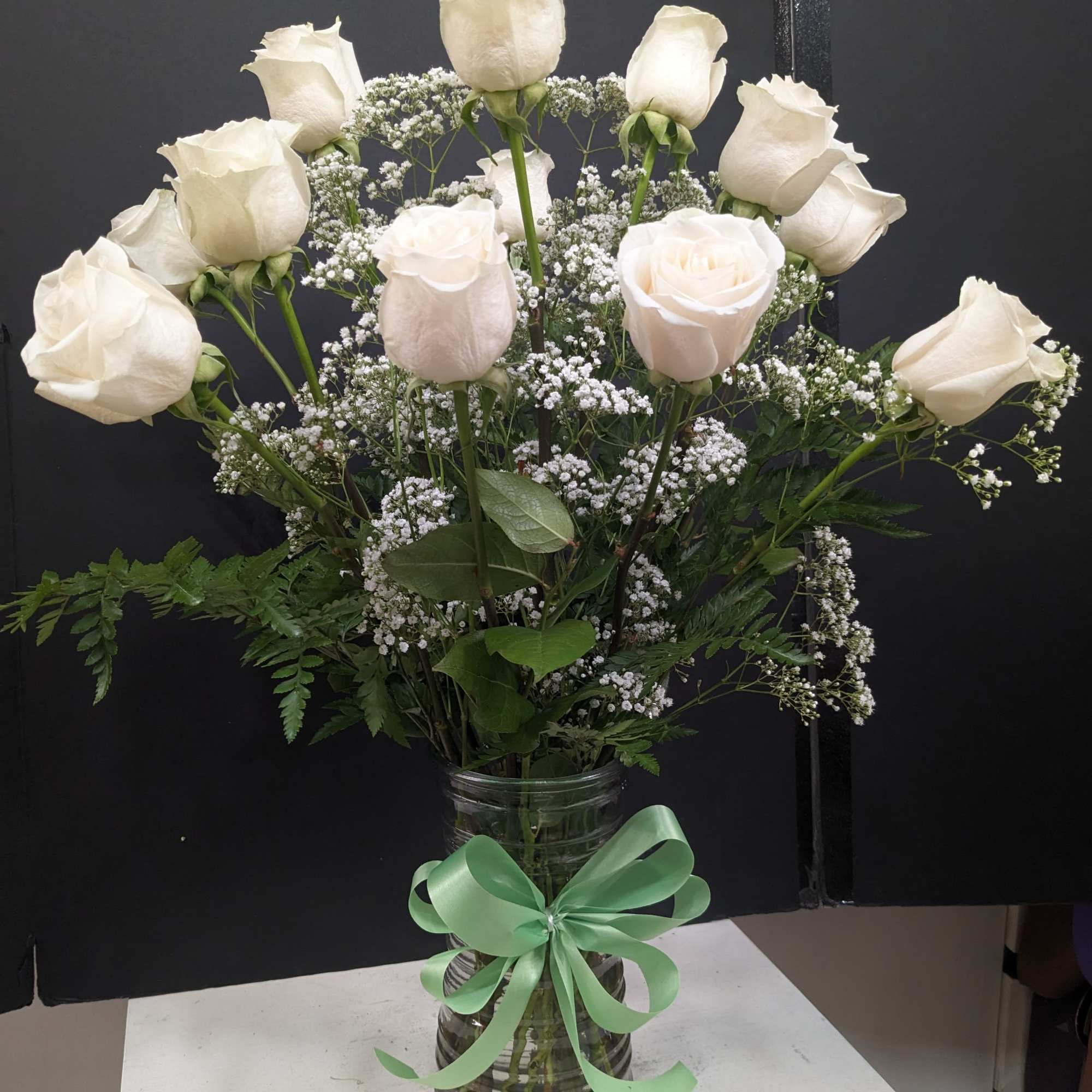 White roses in a glass vase with baby's breath and a green ribbon