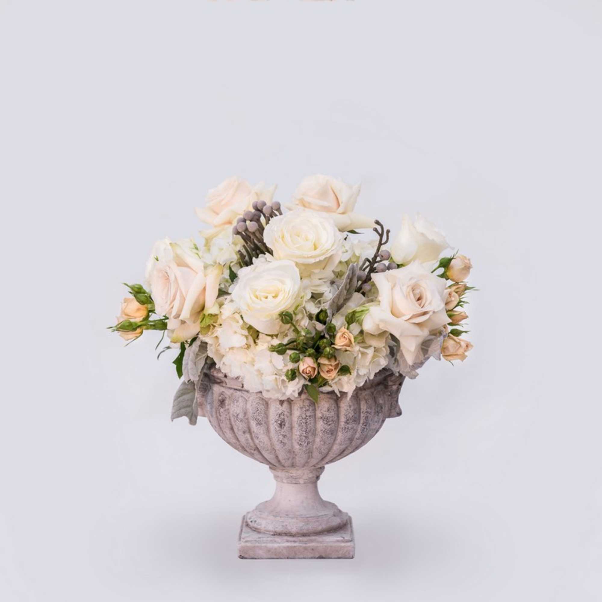 Cream rose arrangement in a stone urn vase