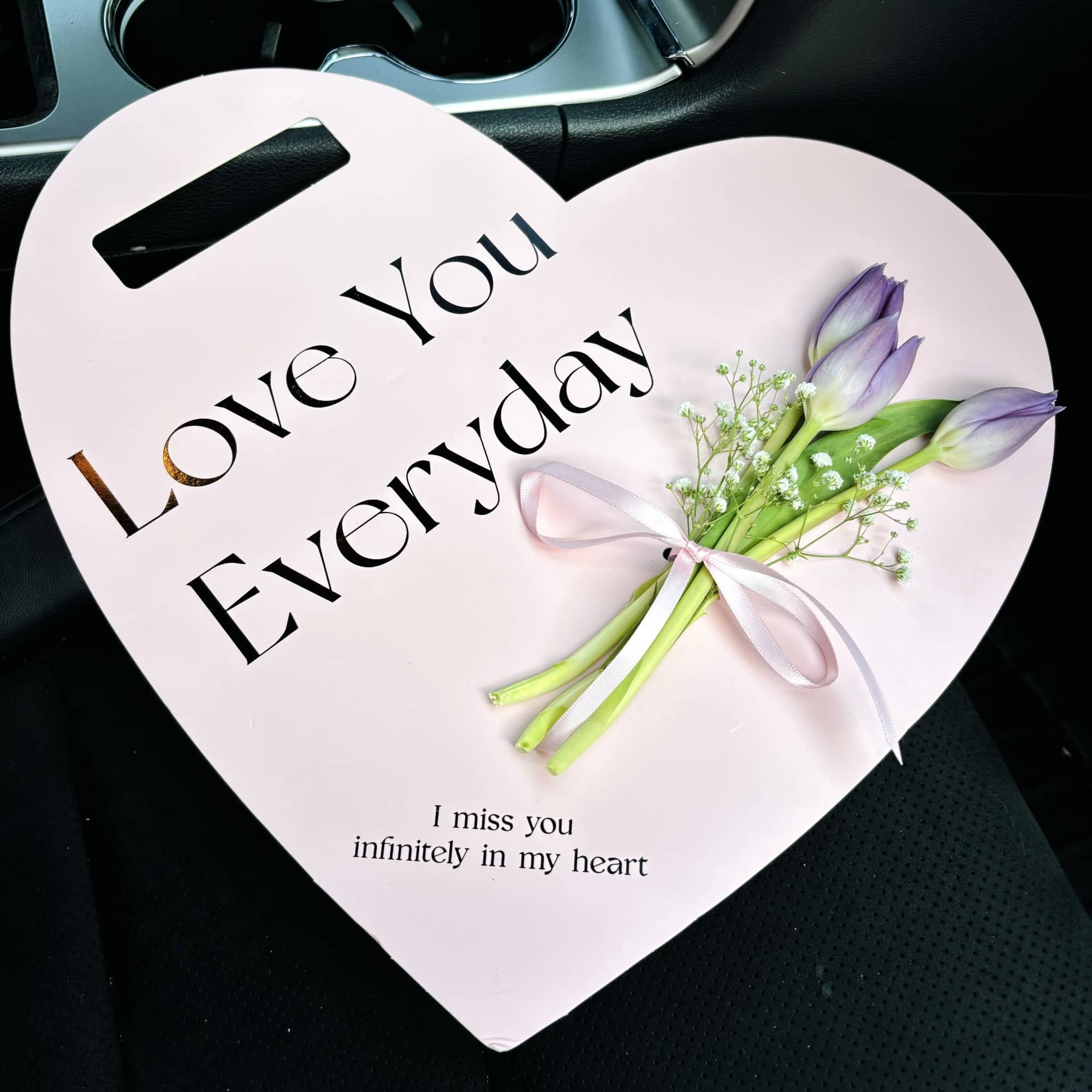 Heart-shaped pink sign with 'Love You Everyday' text and three lavender tulips tied with ribbon.