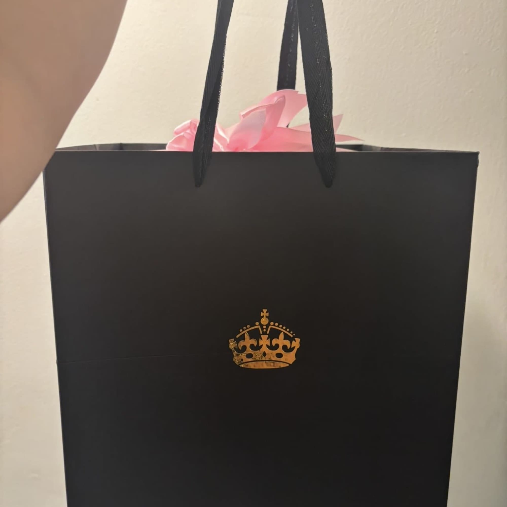 Black gift bag with pink tissue paper and gold crown logo