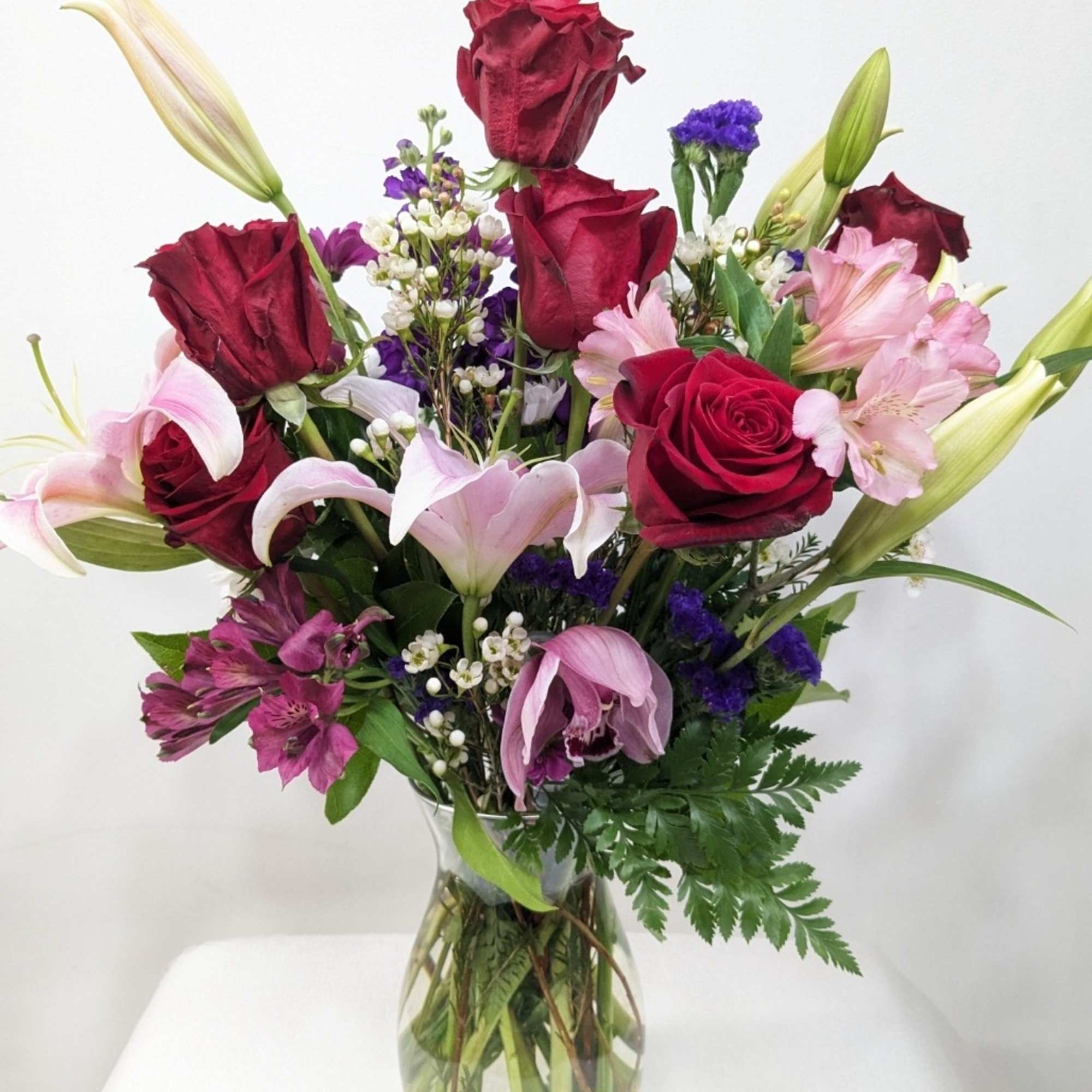 Bouquet of red roses, pink lilies, and purple flowers in a glass vase