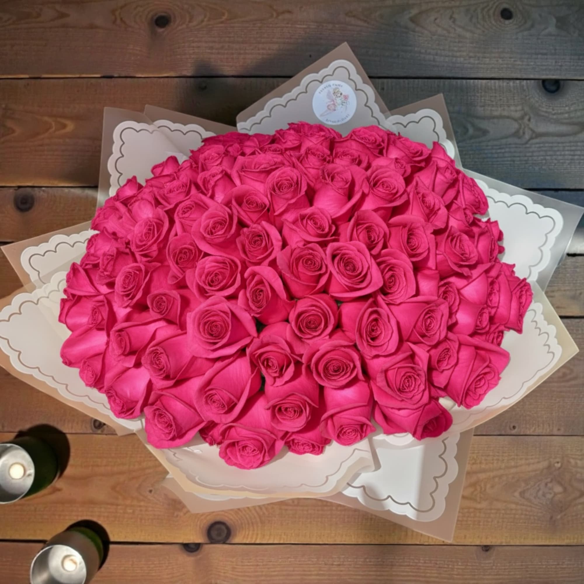 Large round bouquet of hot pink roses wrapped in cream paper on a wooden table.