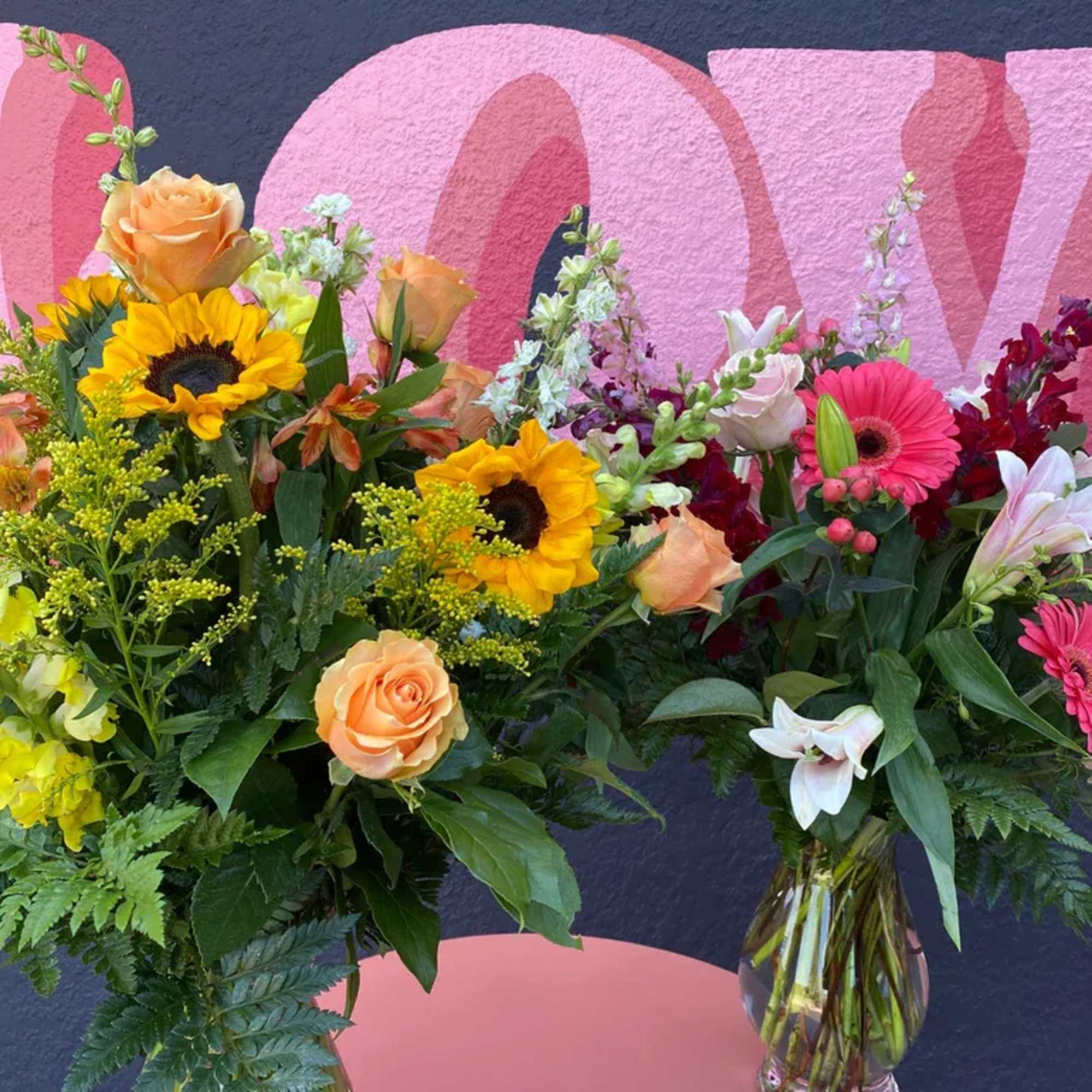 Two colorful mixed flower arrangements in glass vases with sunflowers, roses, and lilies