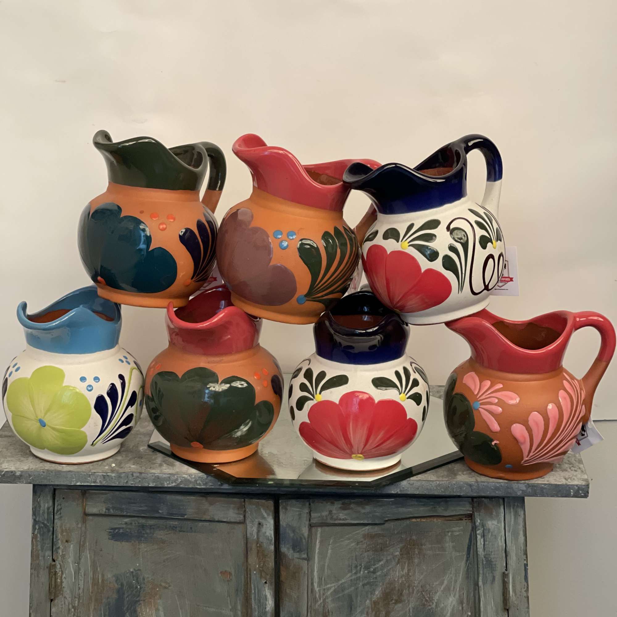 Six colorful painted ceramic pitchers arranged on a cabinet