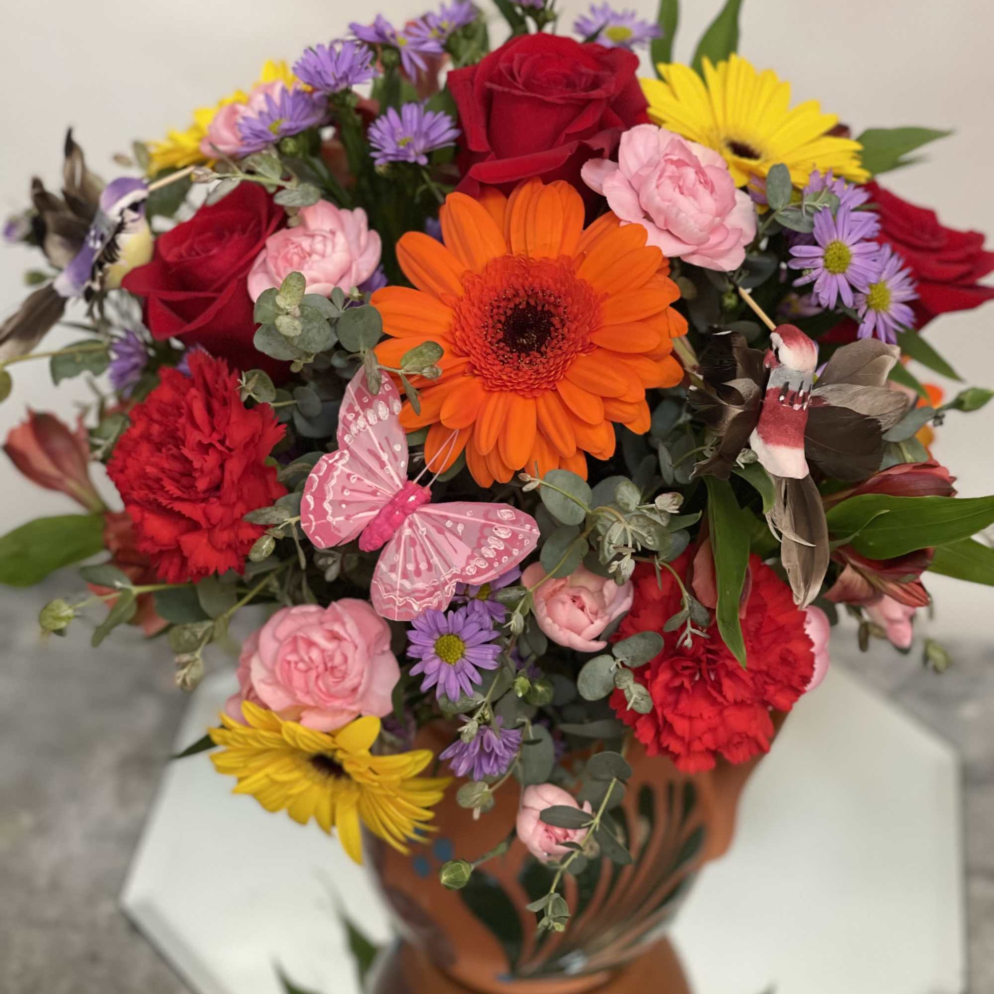 Mixed bouquet with roses, gerbera daisies, and purple daisies in a terracotta vase
