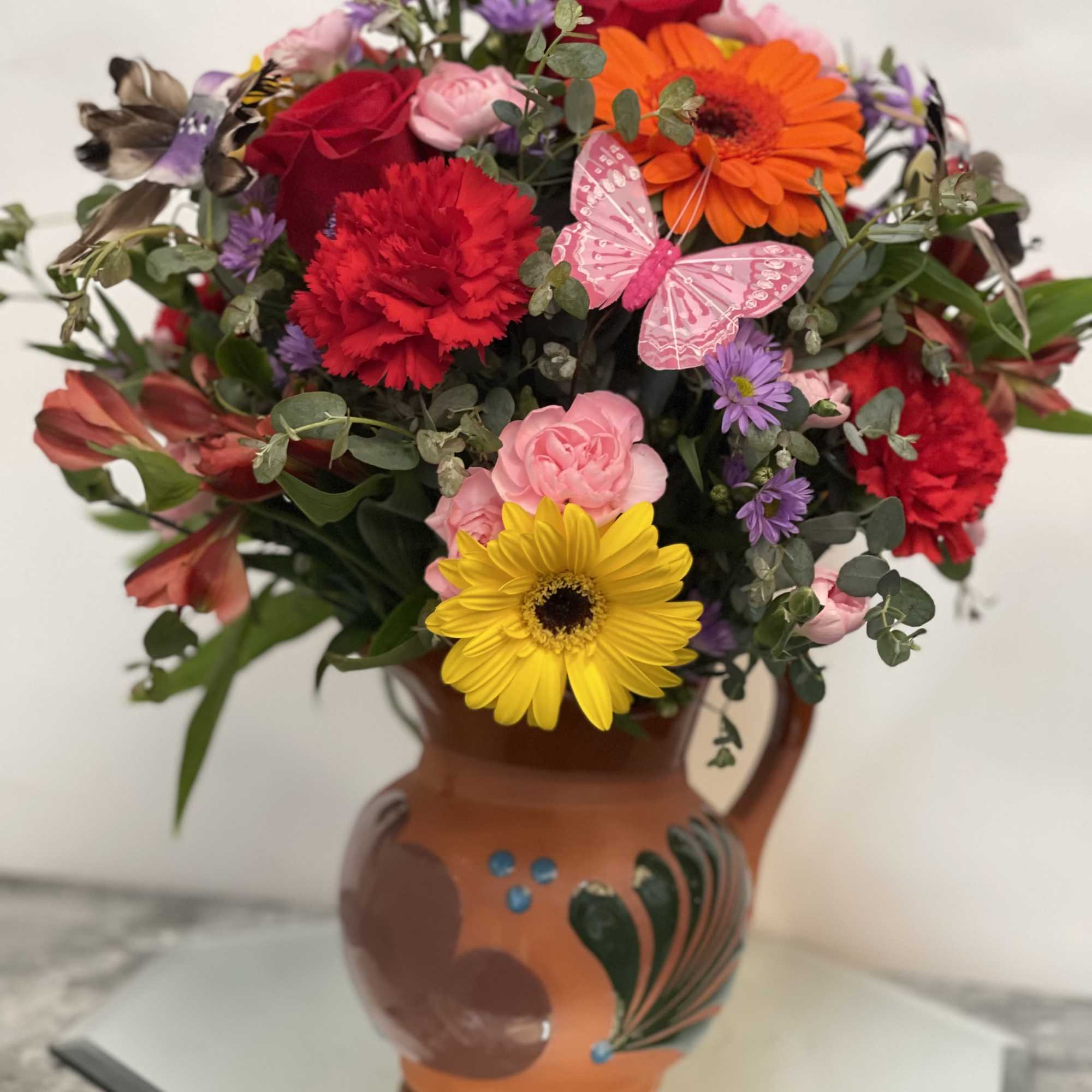 Colorful mixed bouquet in a terracotta vase with a pink butterfly decoration