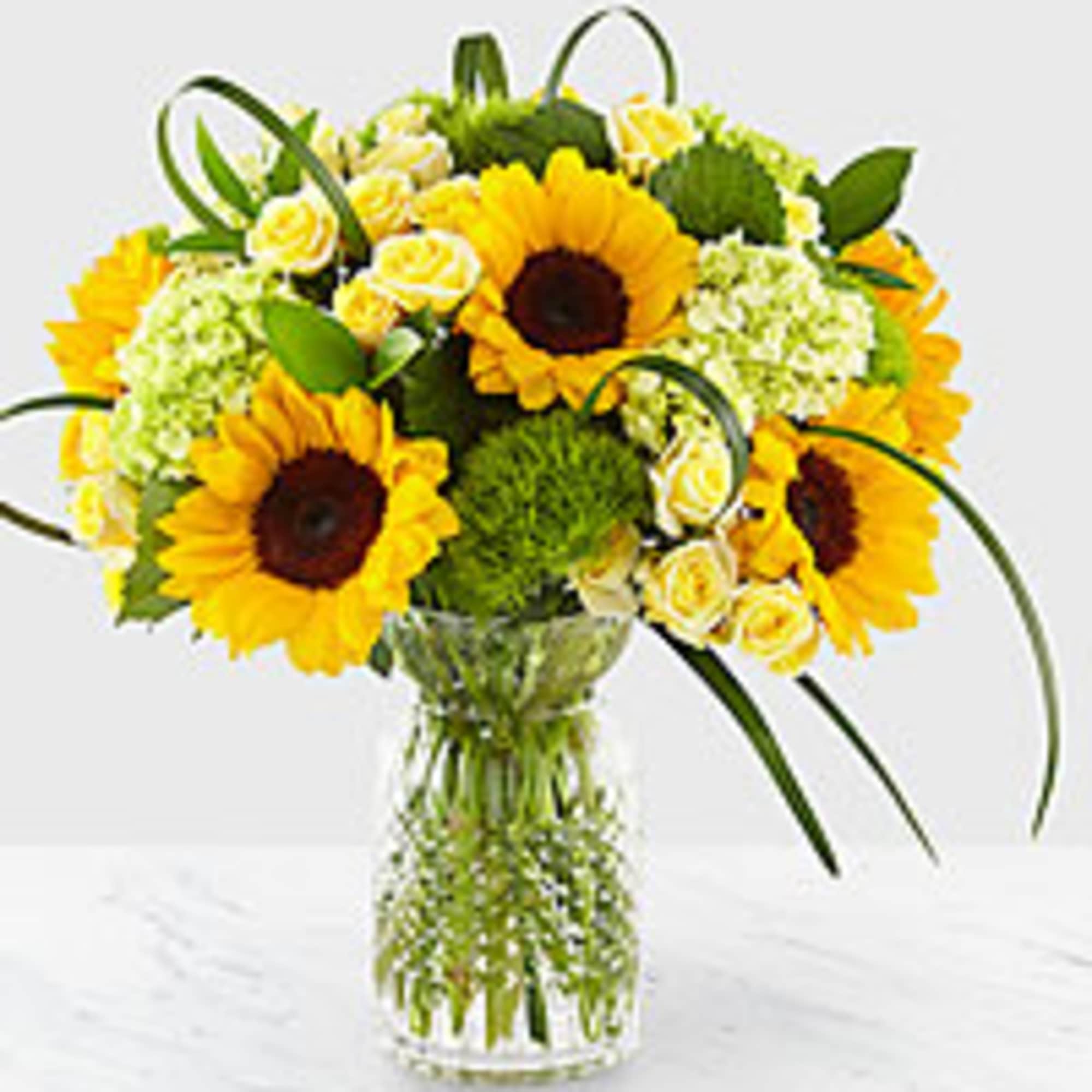 Sunflowers and pale yellow roses arranged in a clear glass vase