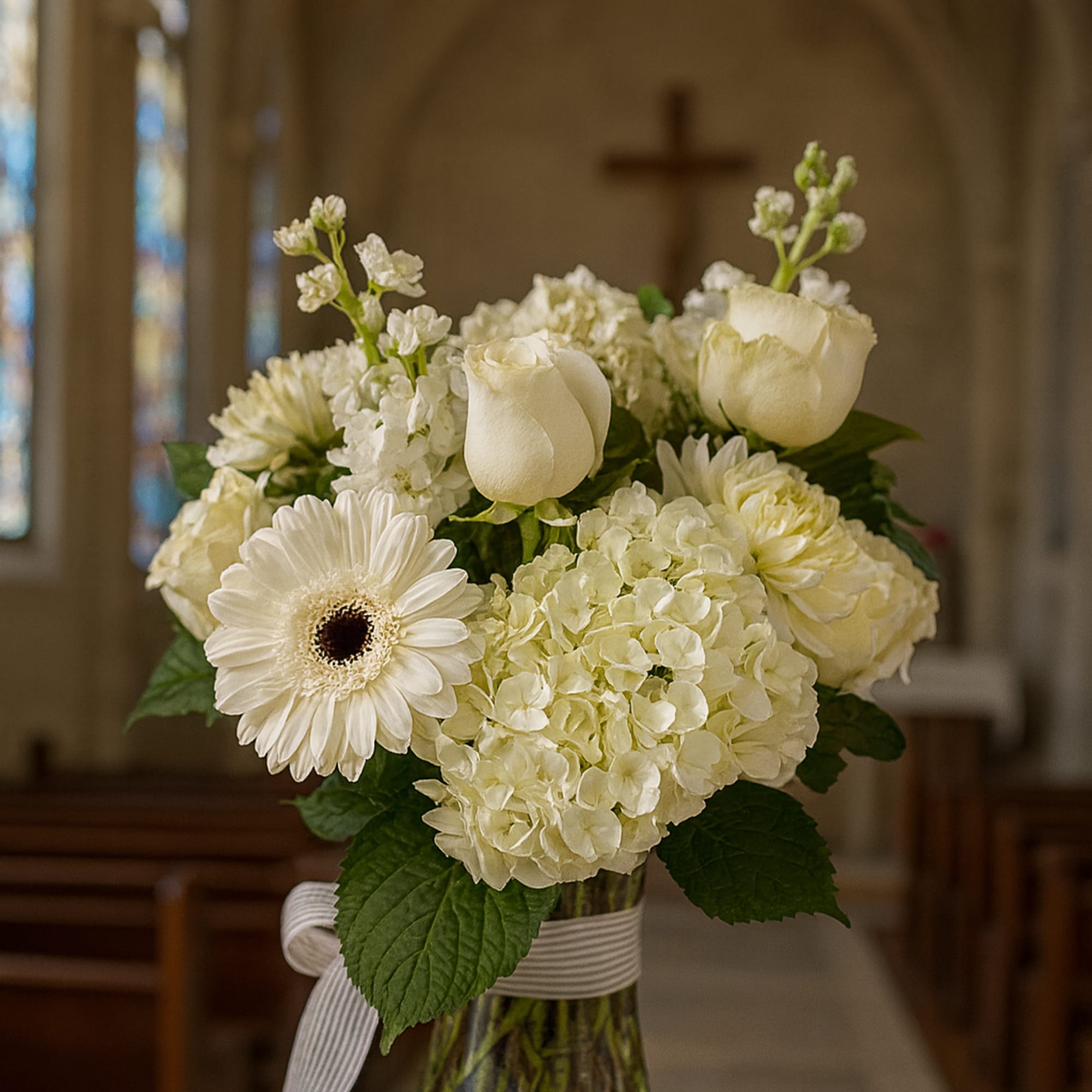White floral arrangement in a glass vase with a ribbon