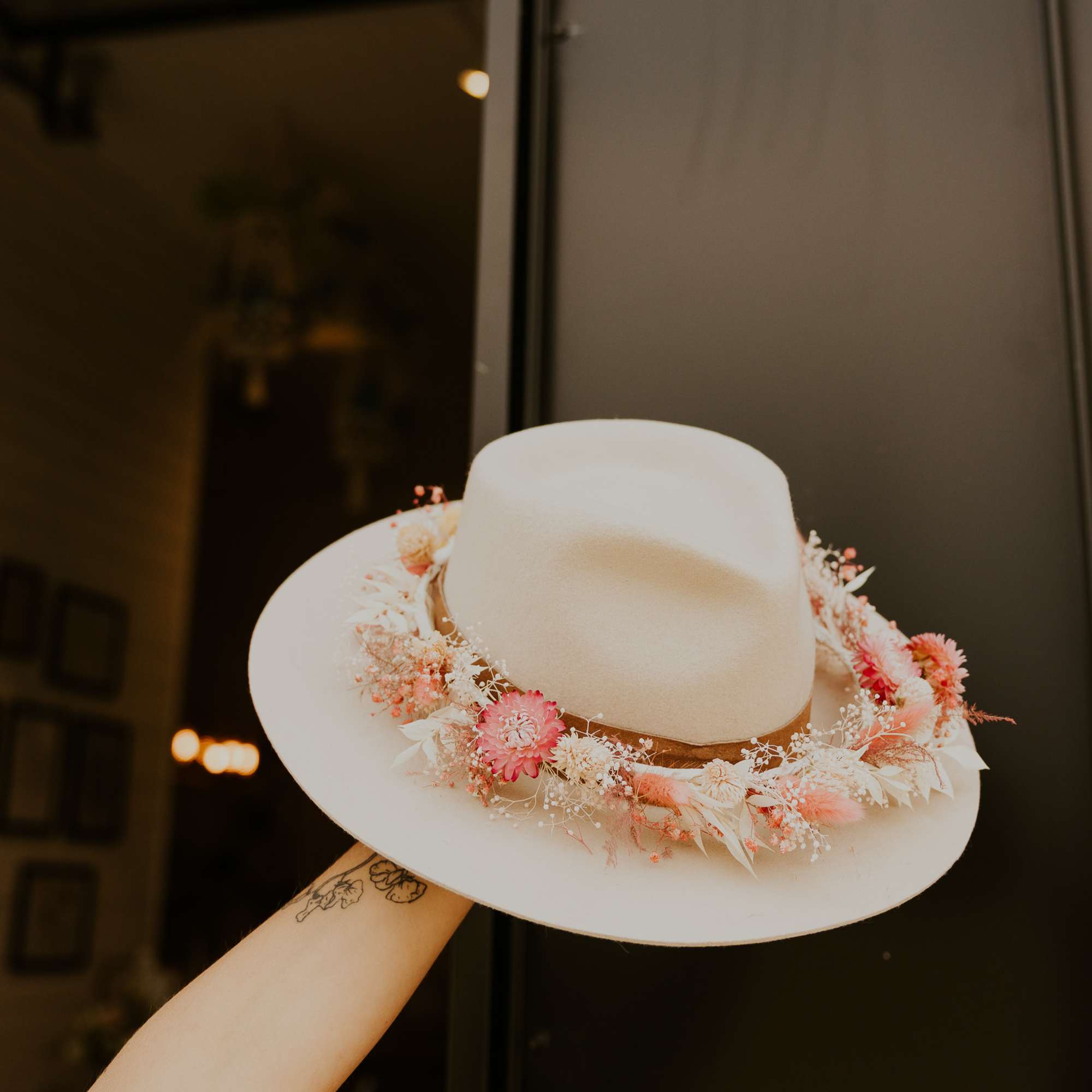 Cream felt hat decorated with a ring of pink and white dried flowers around the brim