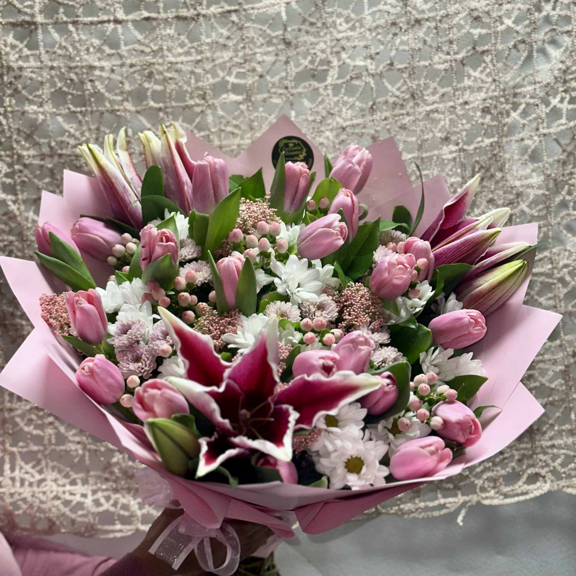Pink tulip bouquet with white daisies and a dark lily in pink wrap