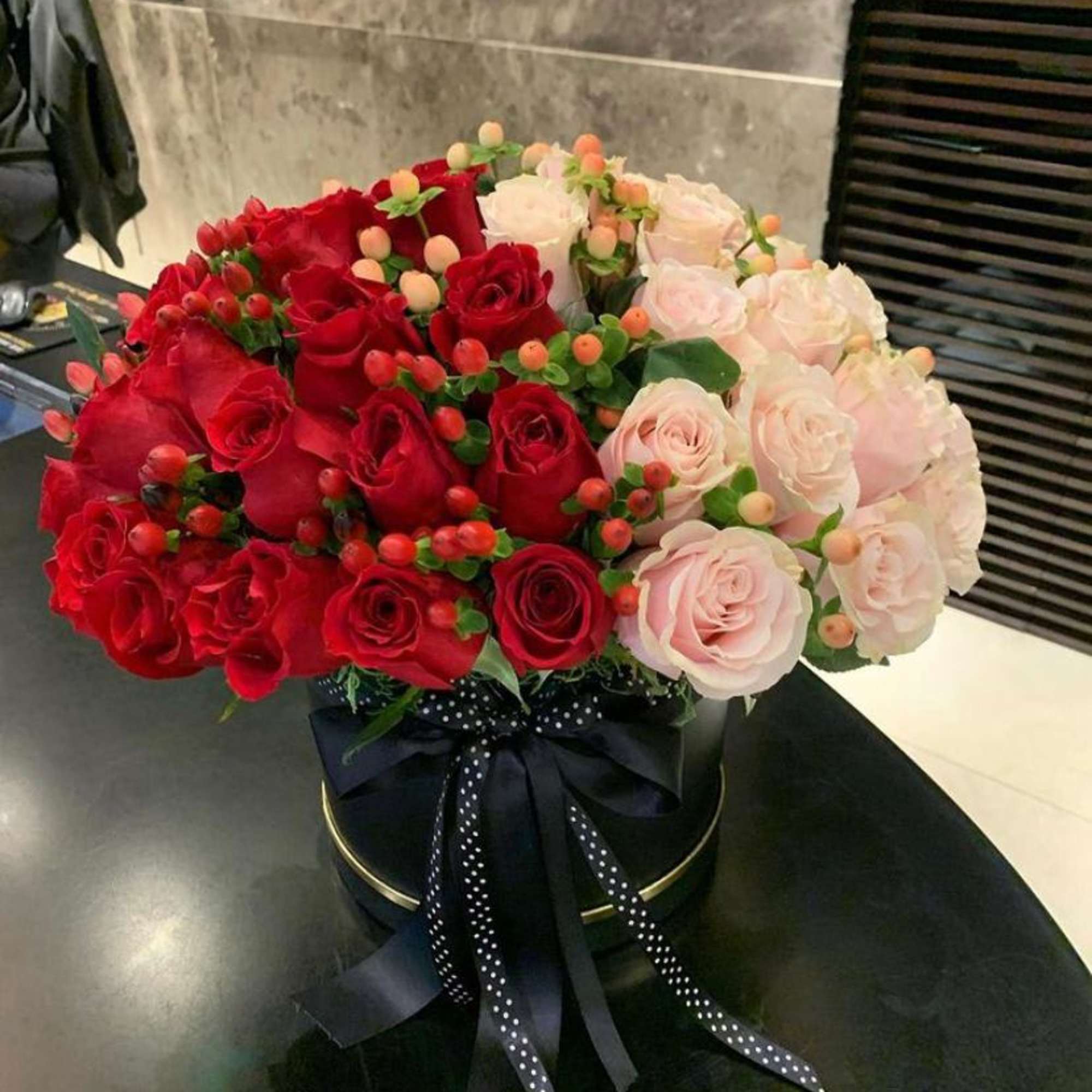Bouquet of red and pale pink roses in a black hatbox with ribbon