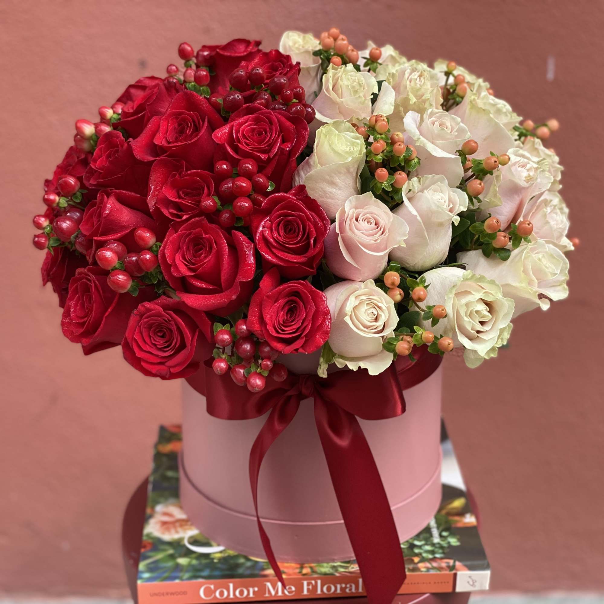 Red and white roses arranged in a pink hat box with a red ribbon