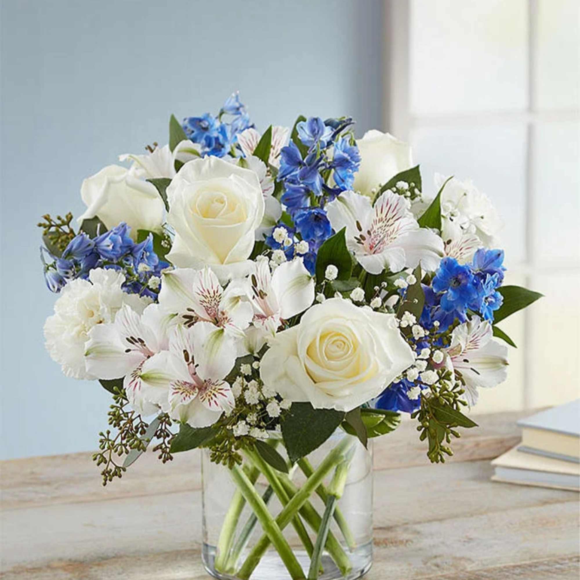 White roses and blue flowers arranged in a clear glass vase