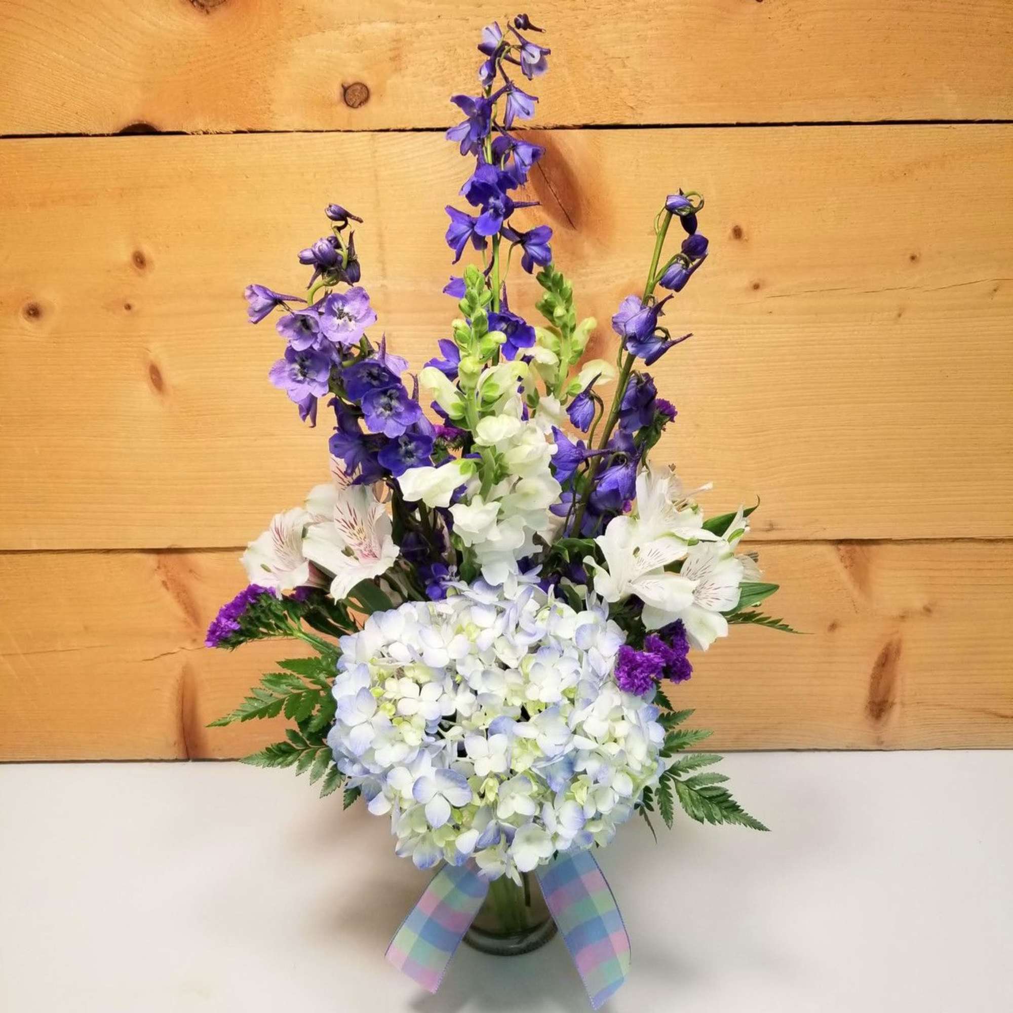 Purple and white floral arrangement in a glass vase with a plaid ribbon