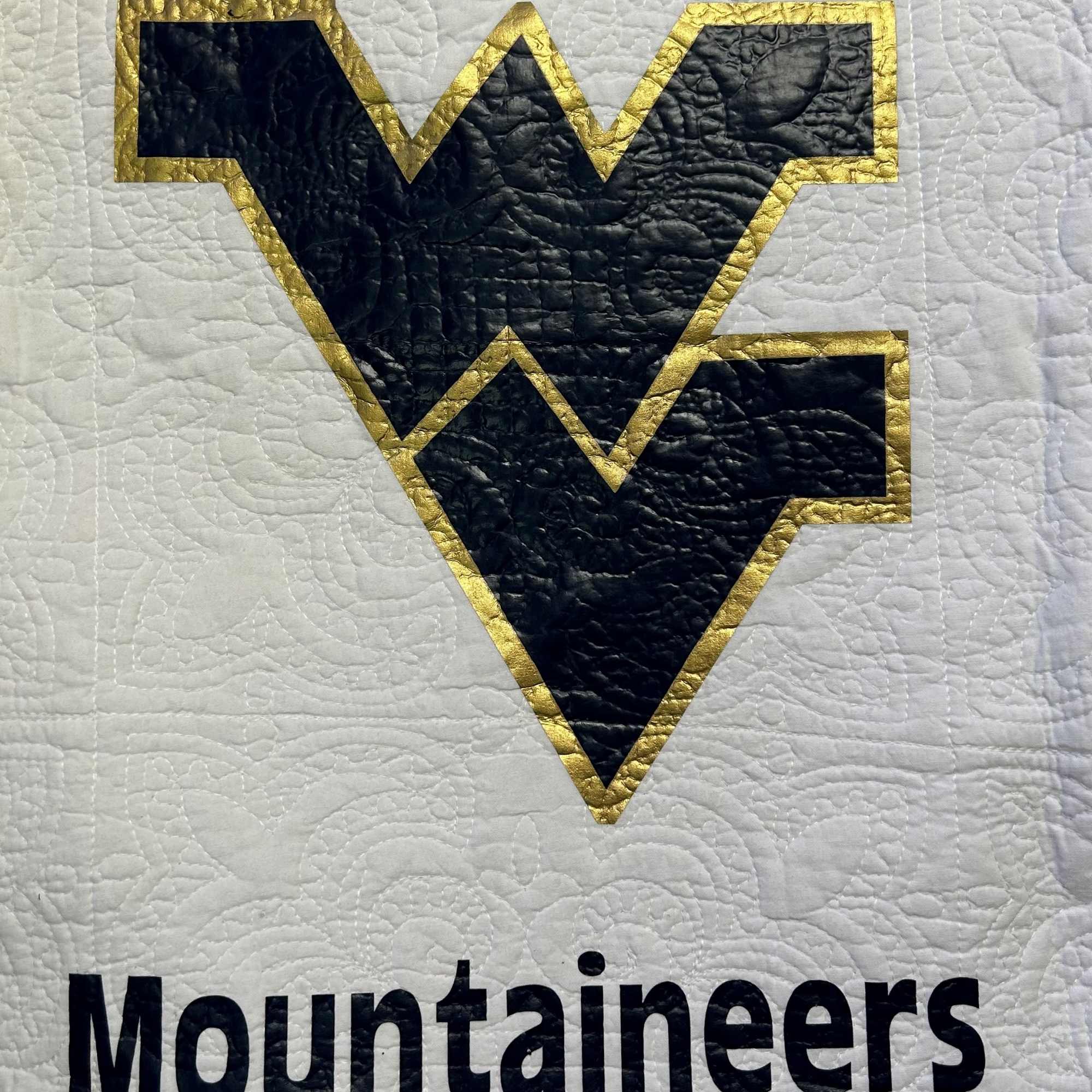 Quilted white fabric with a black and gold Mountaineers logo and text