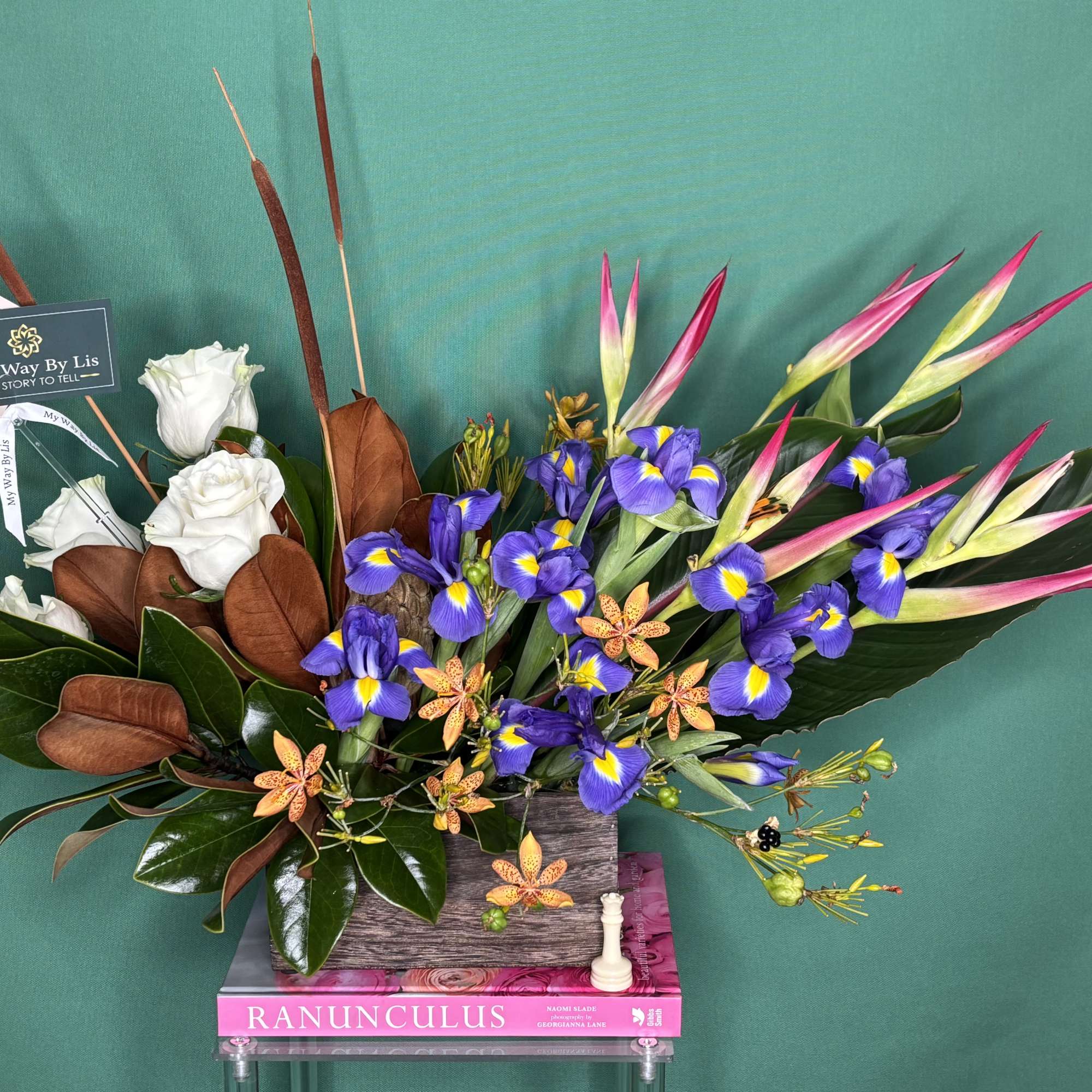 Arrangement of white roses, purple irises, and pink tropical blooms in a rectangular vase