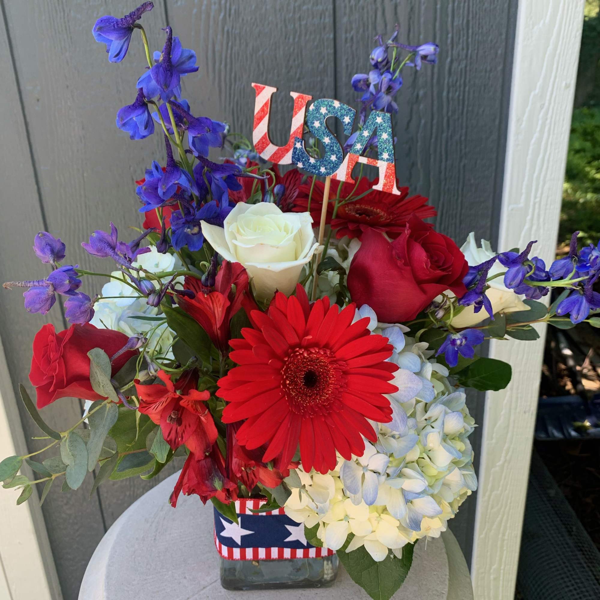 Red, white, and blue flower arrangement in a glass vase with a USA pick