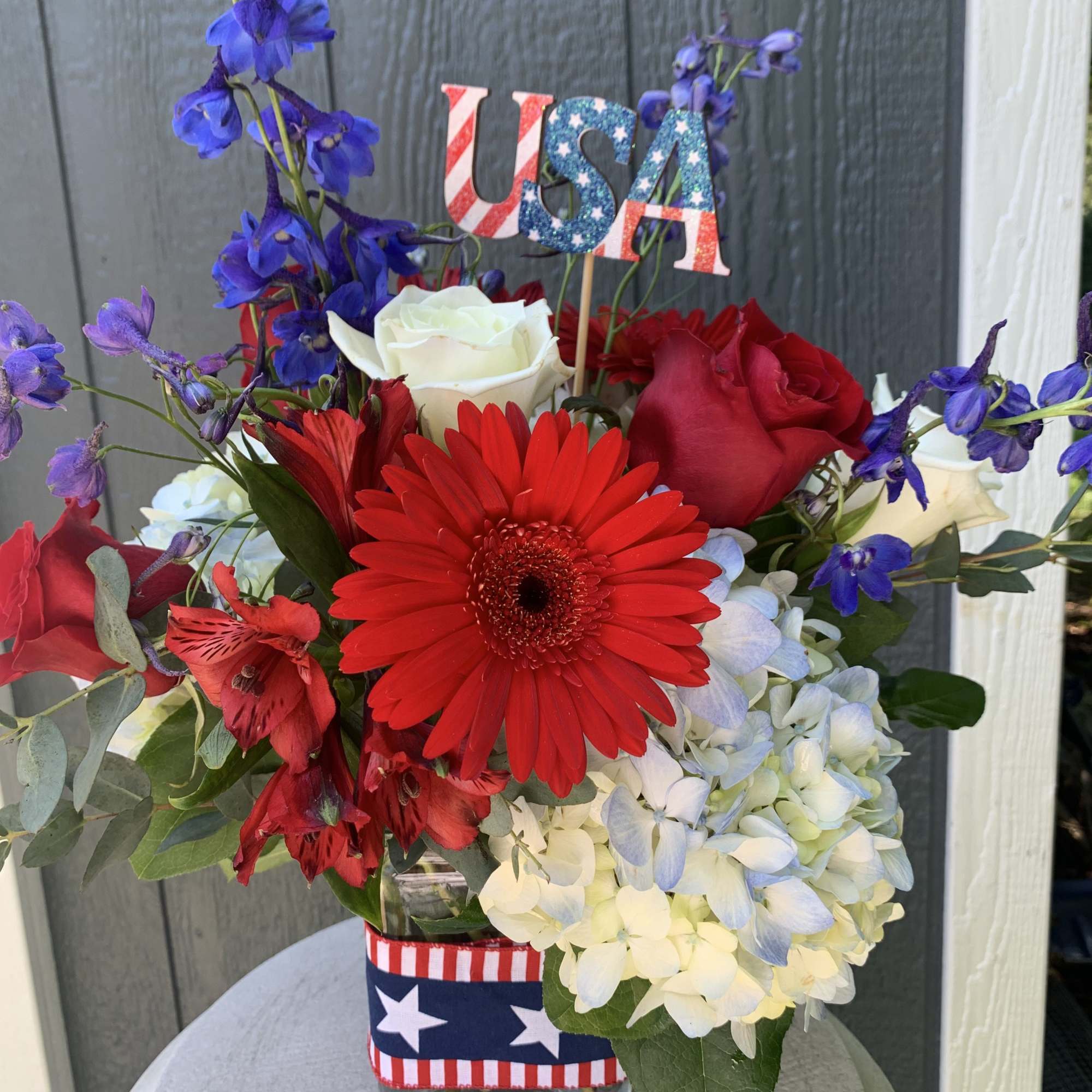 Red, white, and blue floral arrangement in a glass vase with a USA topper