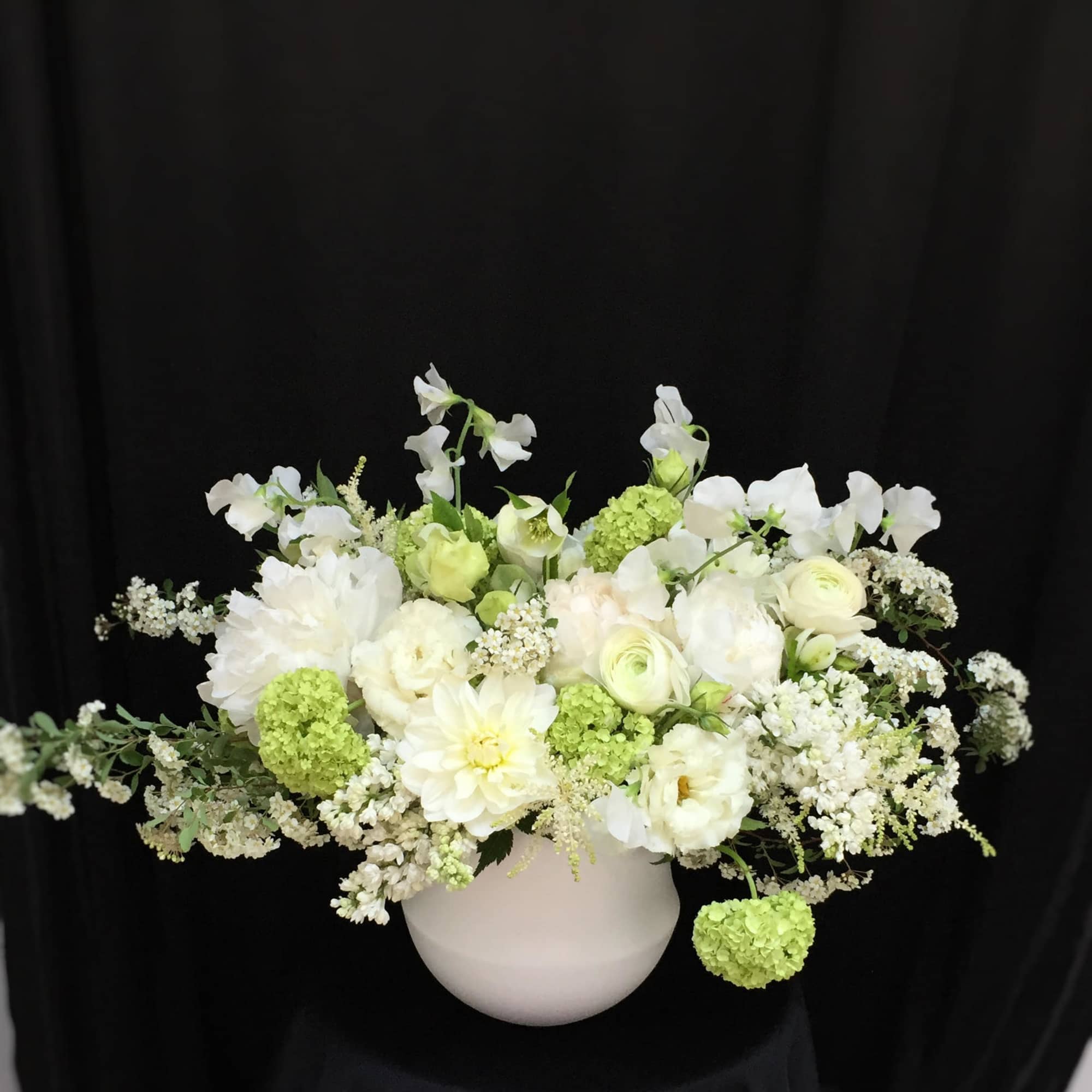 White and pale green floral arrangement in a round white vase