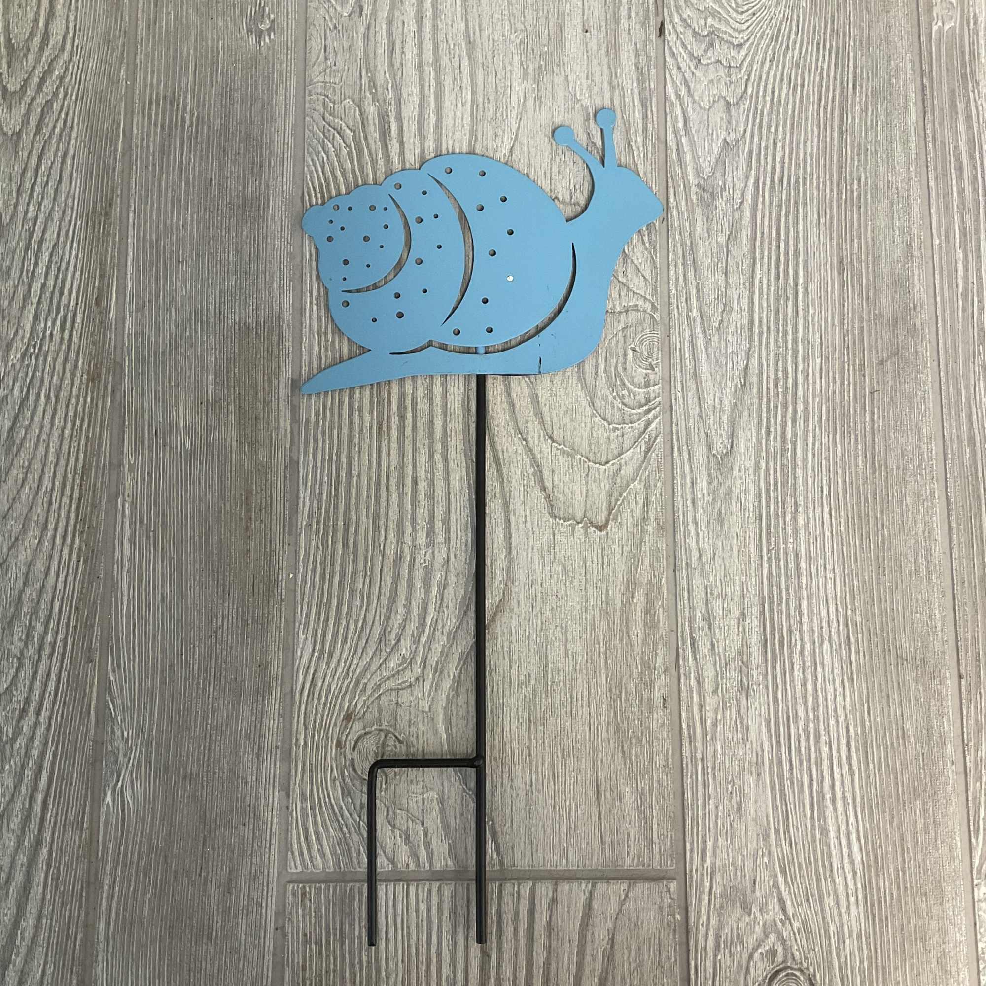 Blue snail-shaped metal garden stake on a wood floor