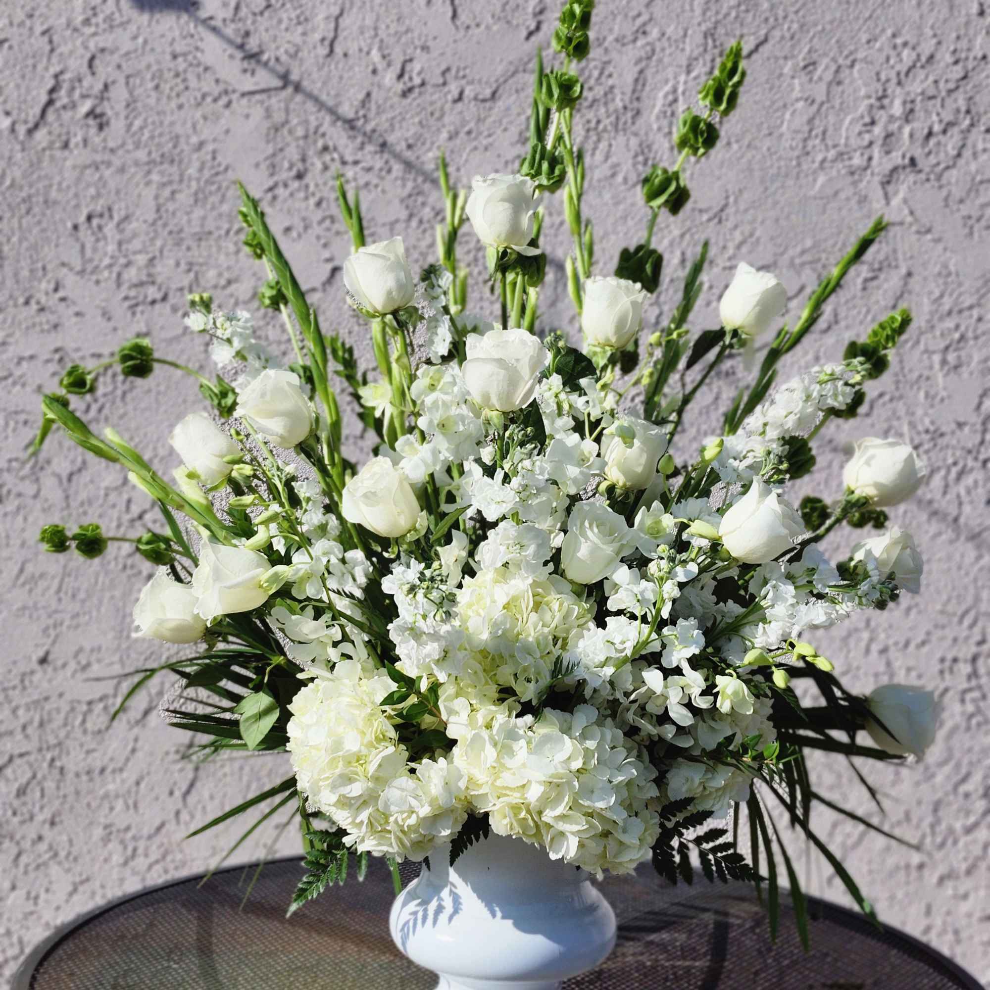White floral arrangement in a white vase with tall stems and clustered blooms