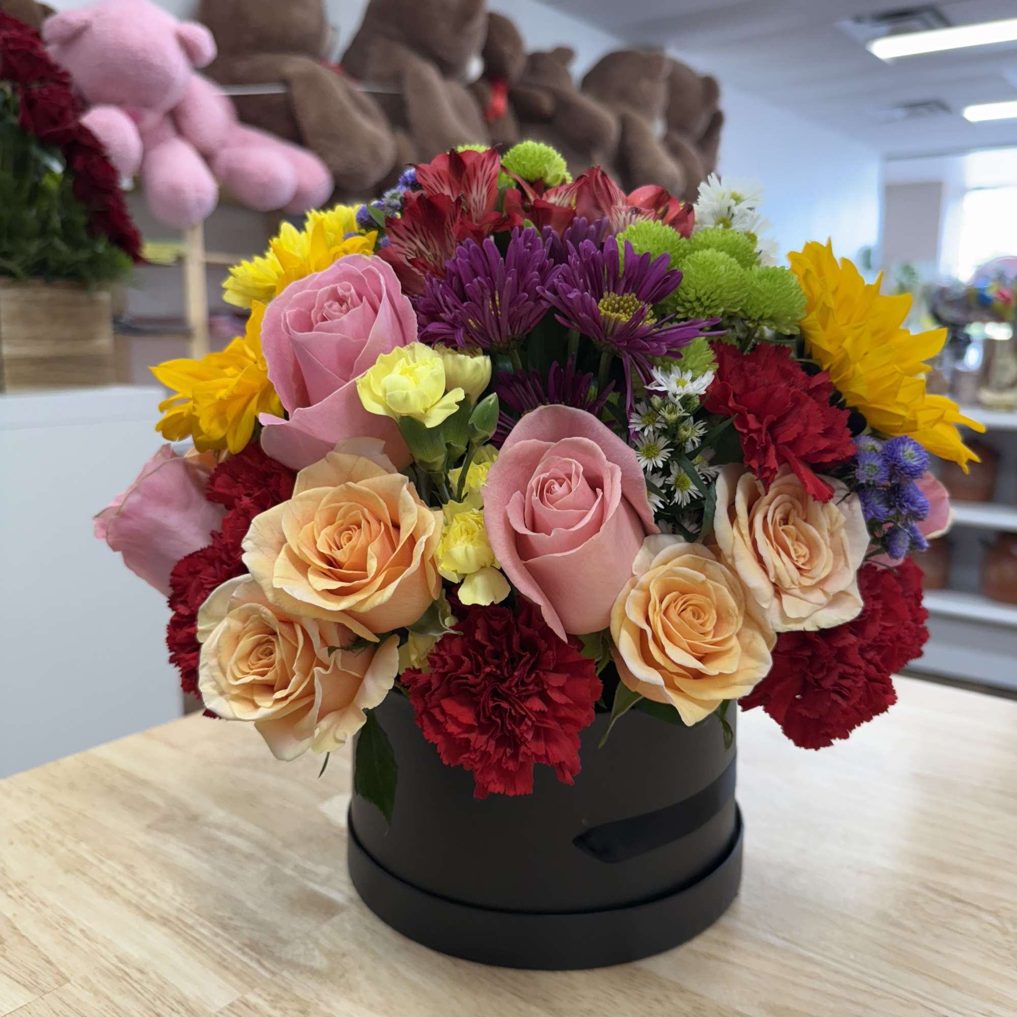 Mixed bouquet of roses, carnations, and daisies in a black hat box