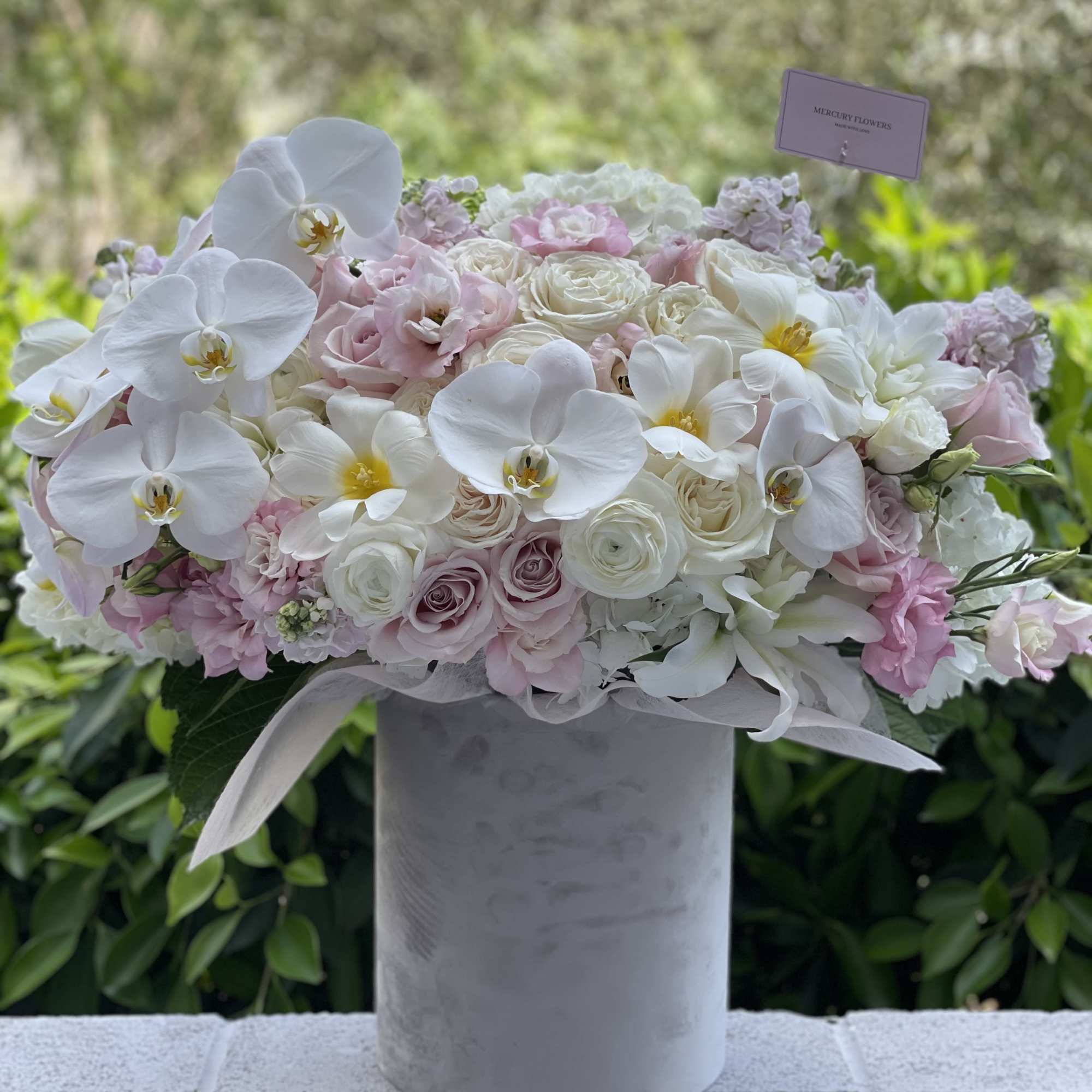 White and blush floral arrangement in a gray vase with orchids and roses