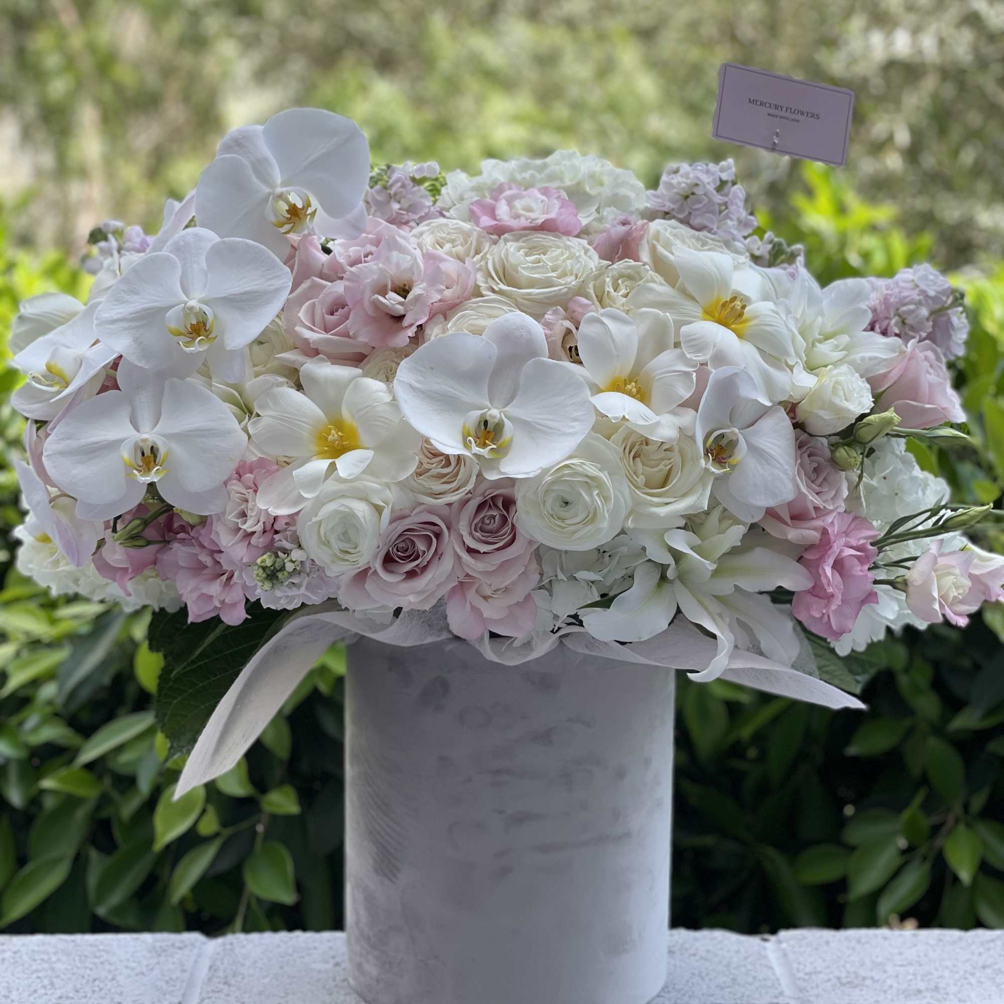 White orchids and blush roses arranged in a tall gray vase