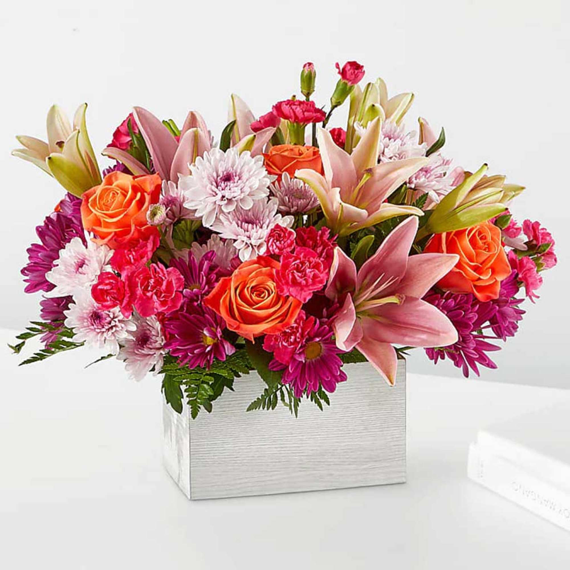 Mixed bouquet of orange roses, pink lilies, and purple daisies in a silver box