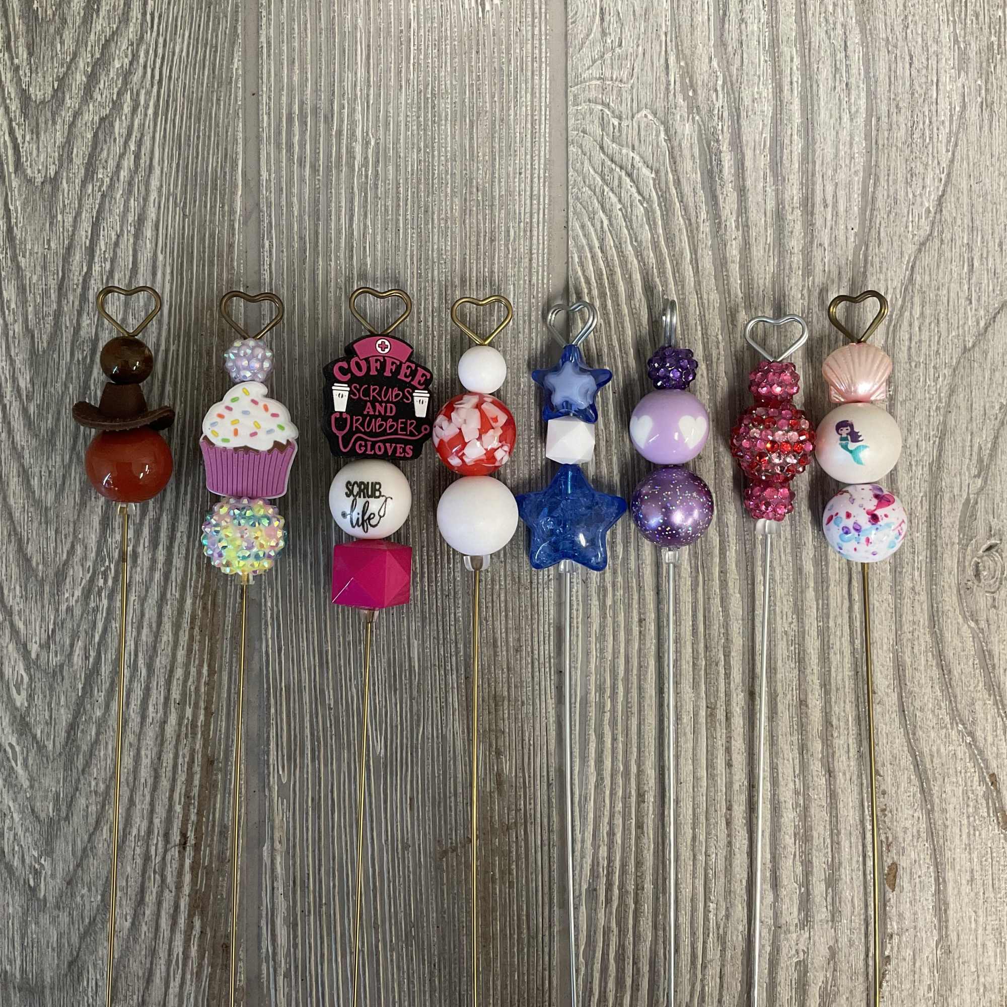 Decorative beaded picks with heart-shaped toppers arranged on a wood surface.