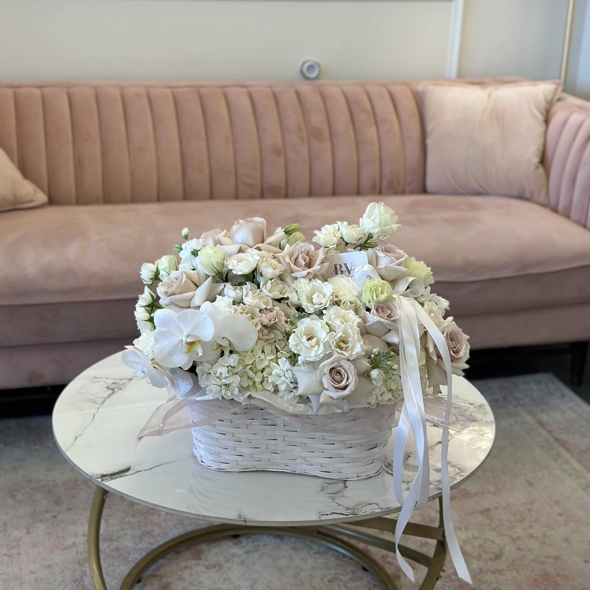 Cream and blush floral arrangement in a white basket with ribbon
