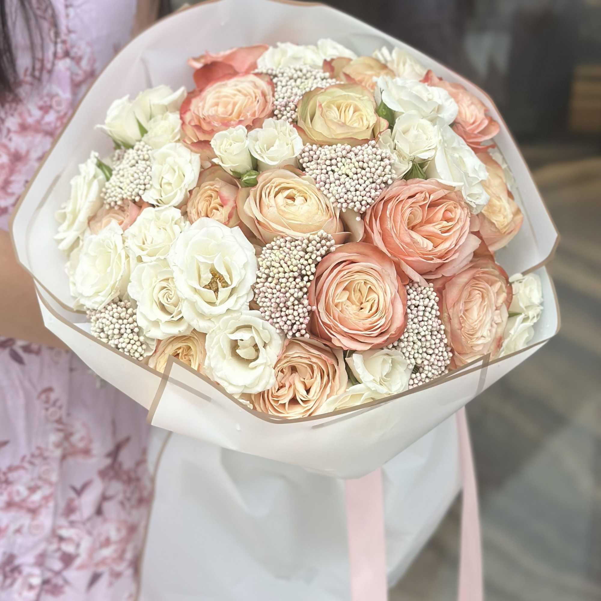 Bouquet of peach and white roses wrapped in pale paper