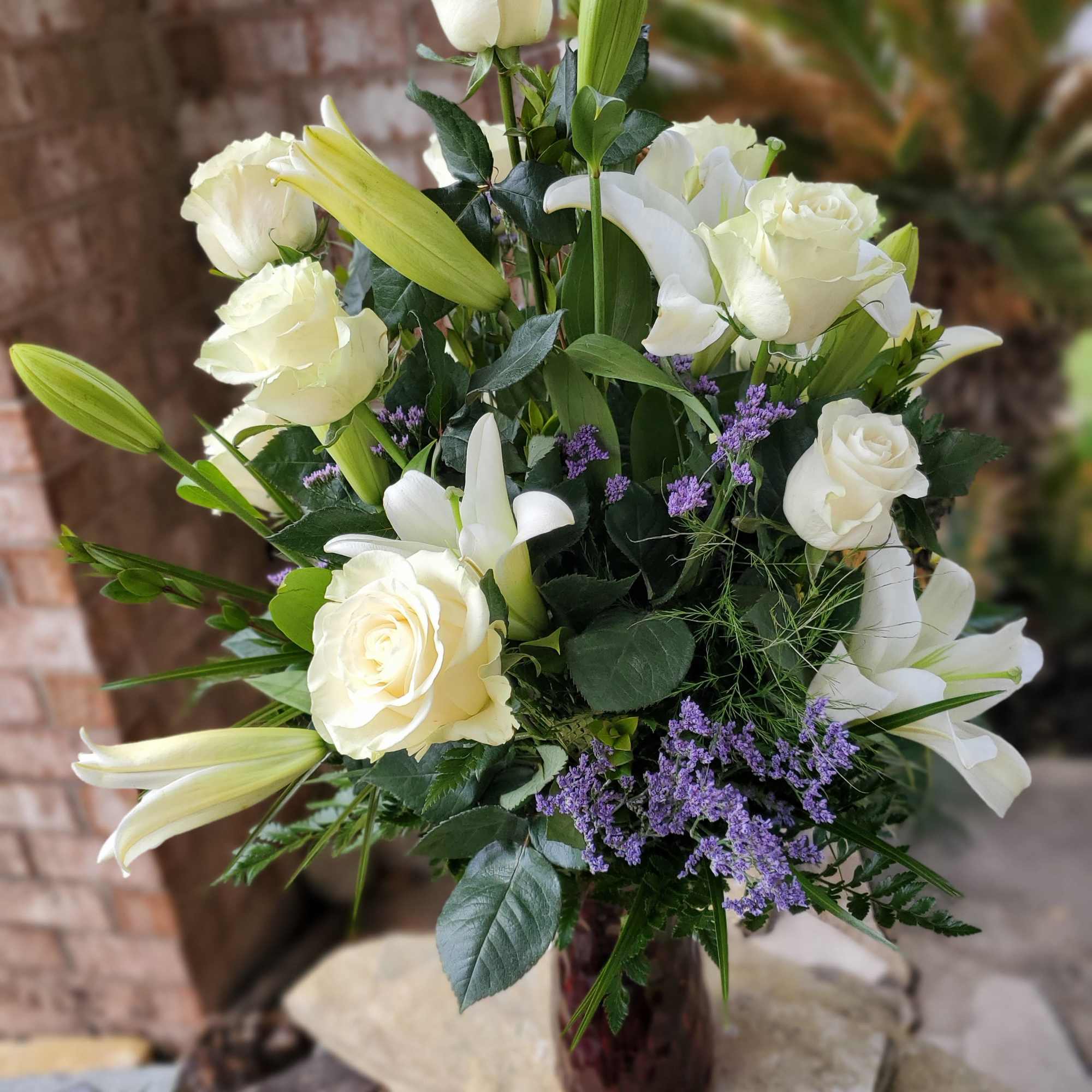 White roses and lilies arranged in a glass vase with purple filler flowers
