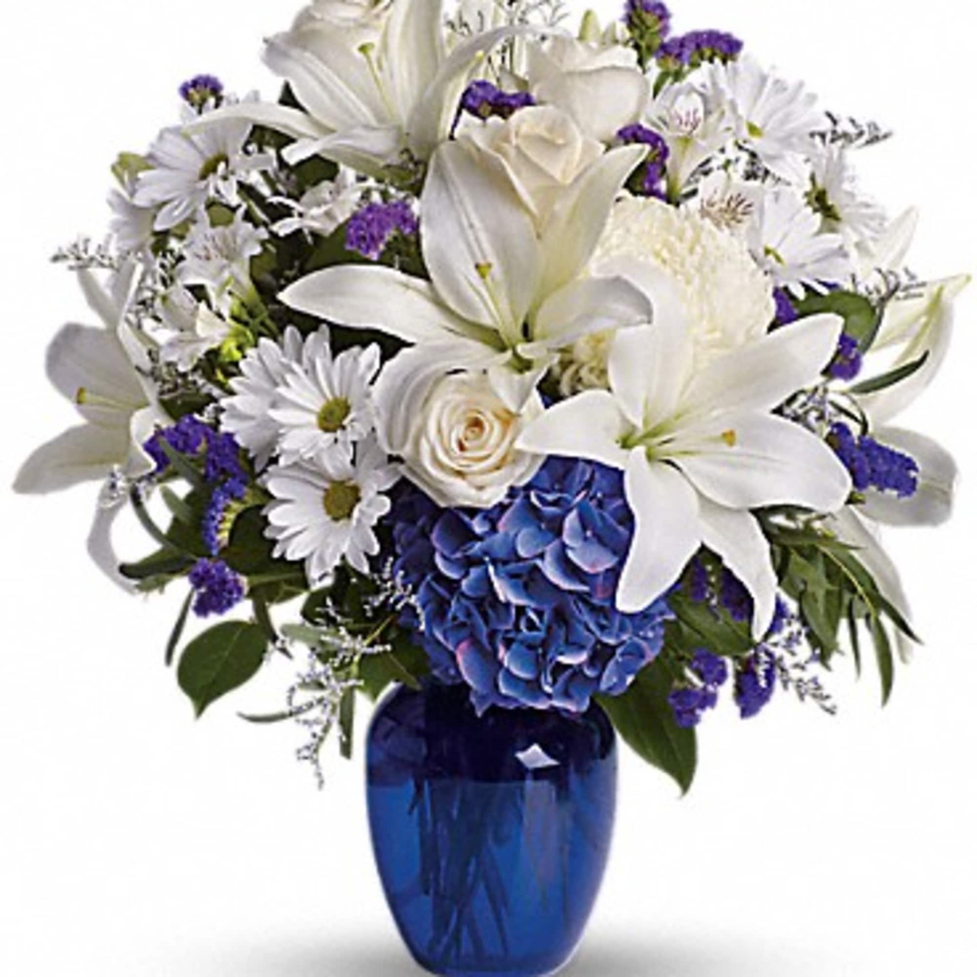 White lilies and daisies with blue hydrangea in a cobalt vase
