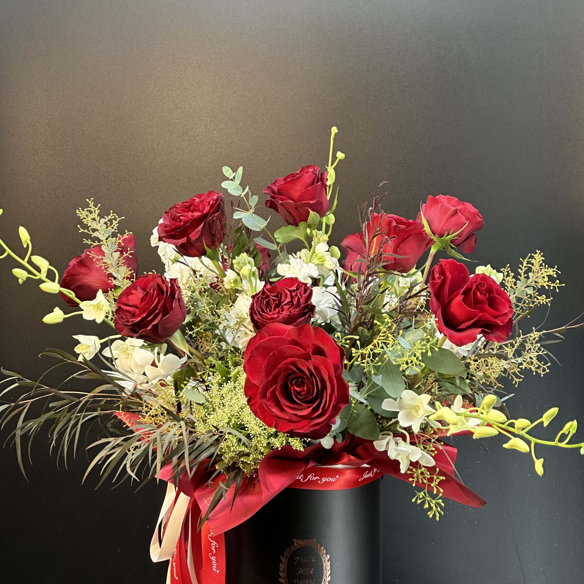 Red roses and white orchids arranged in a black hat box with a red ribbon.