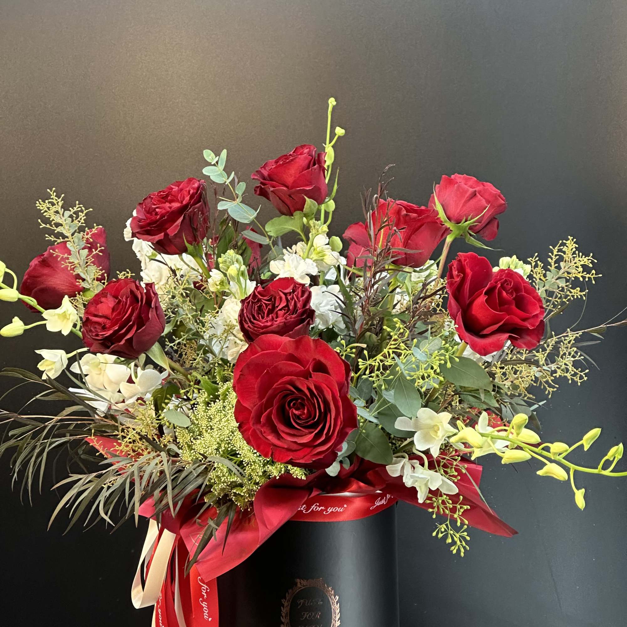 Red roses and white orchids in a black hatbox with a red ribbon