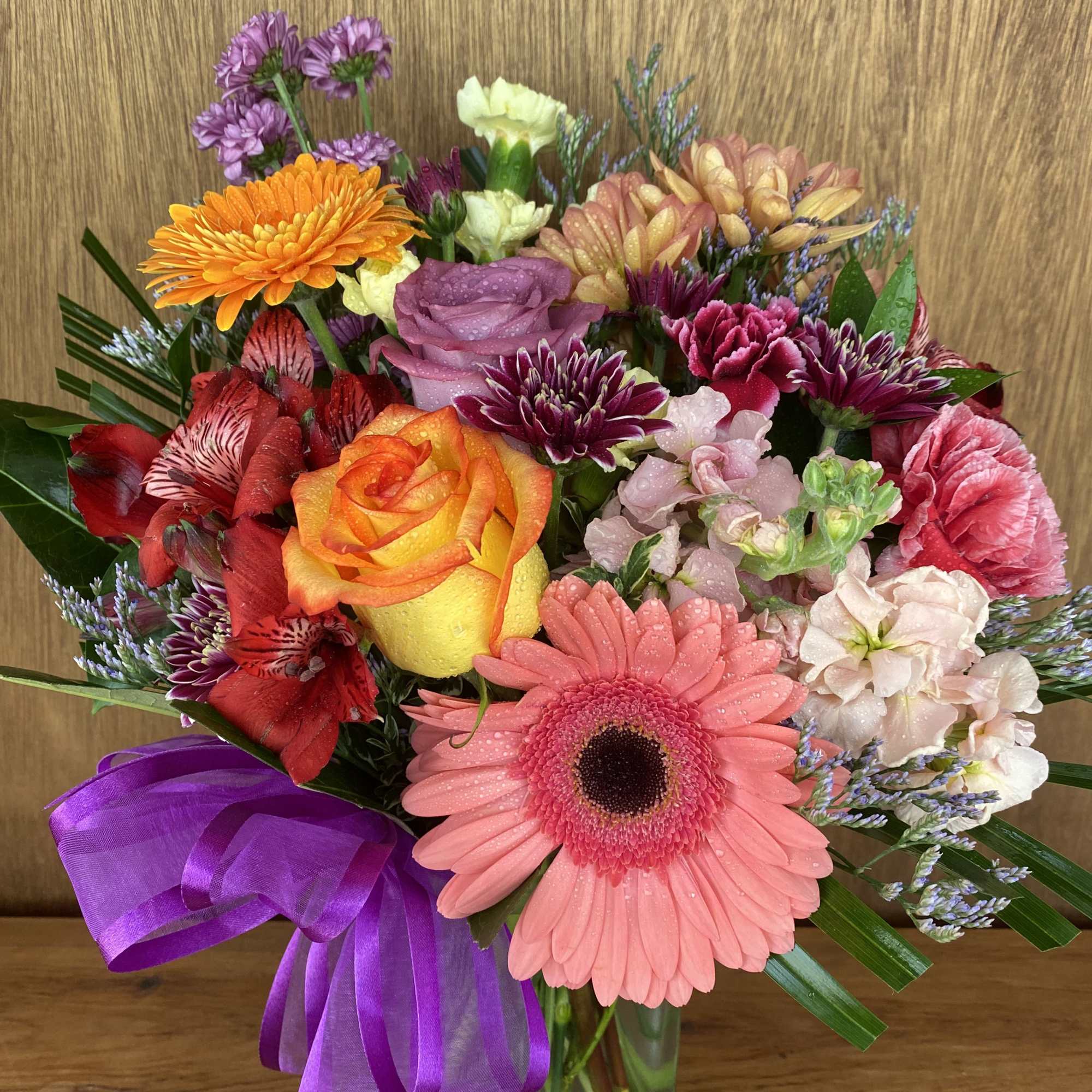 Mixed bouquet of colorful flowers in a glass vase with a purple ribbon
