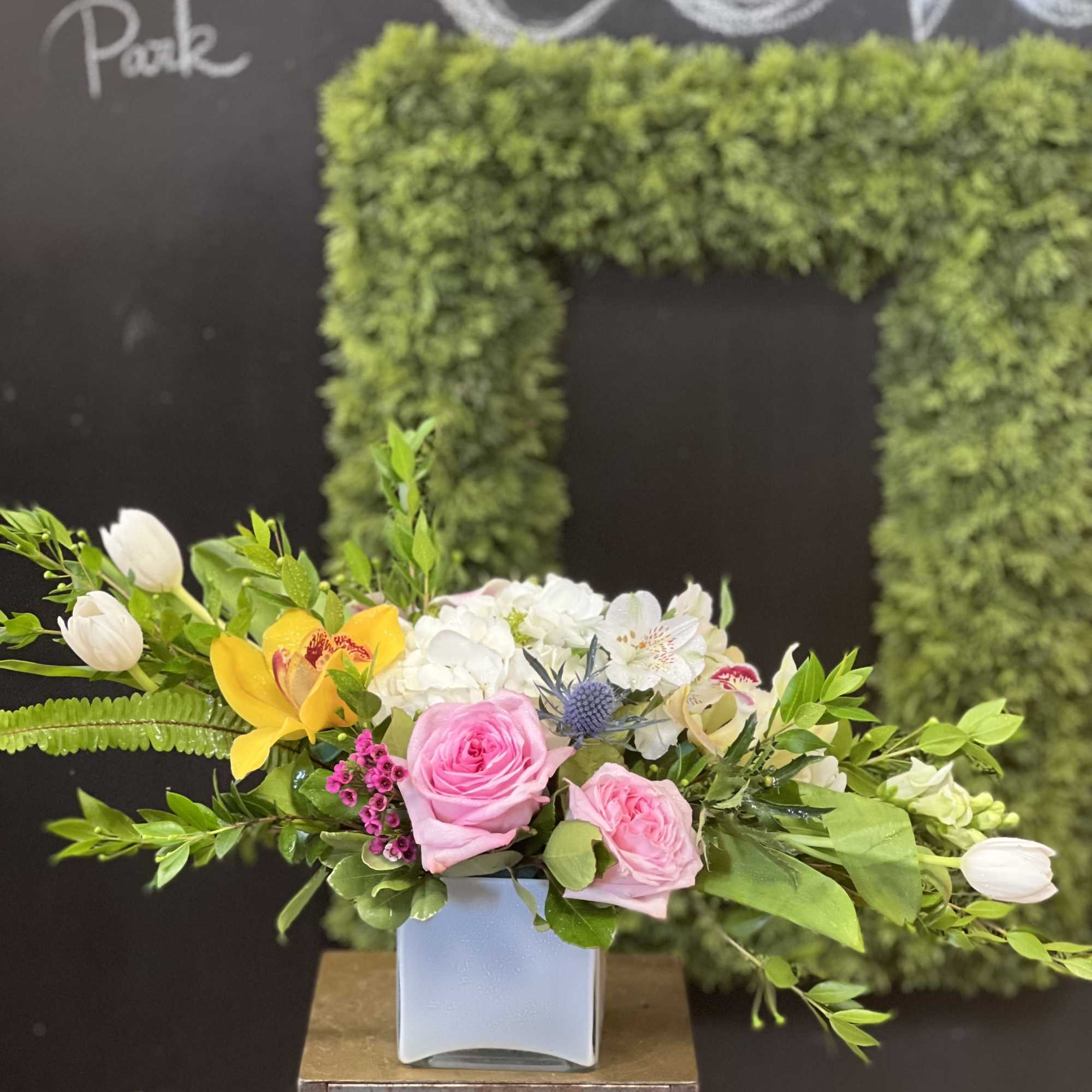 Mixed bouquet of pink roses, white blooms, and yellow orchids in a square vase