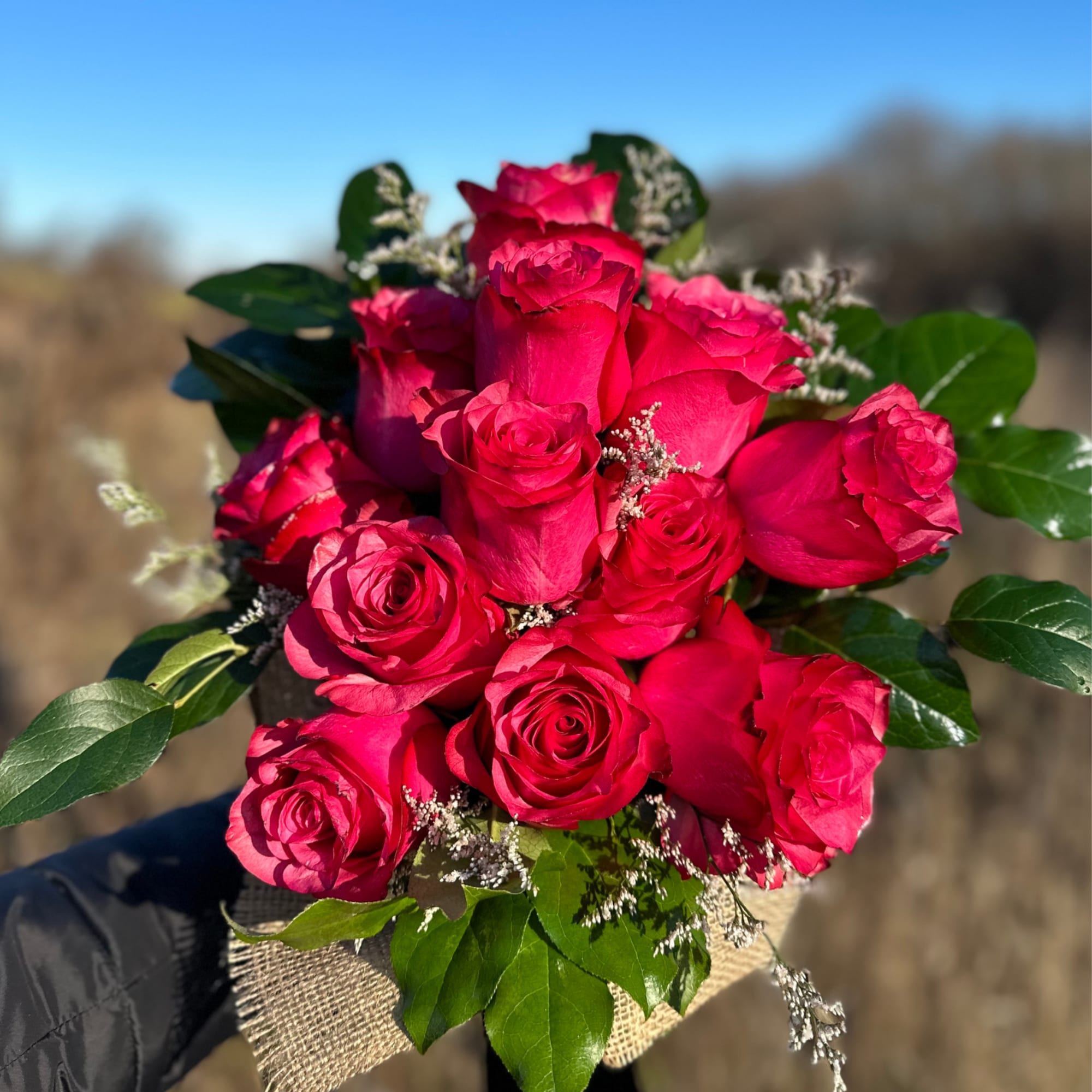 Hand-tied bouquet of bright pink roses with small white filler flowers wrapped in burlap.