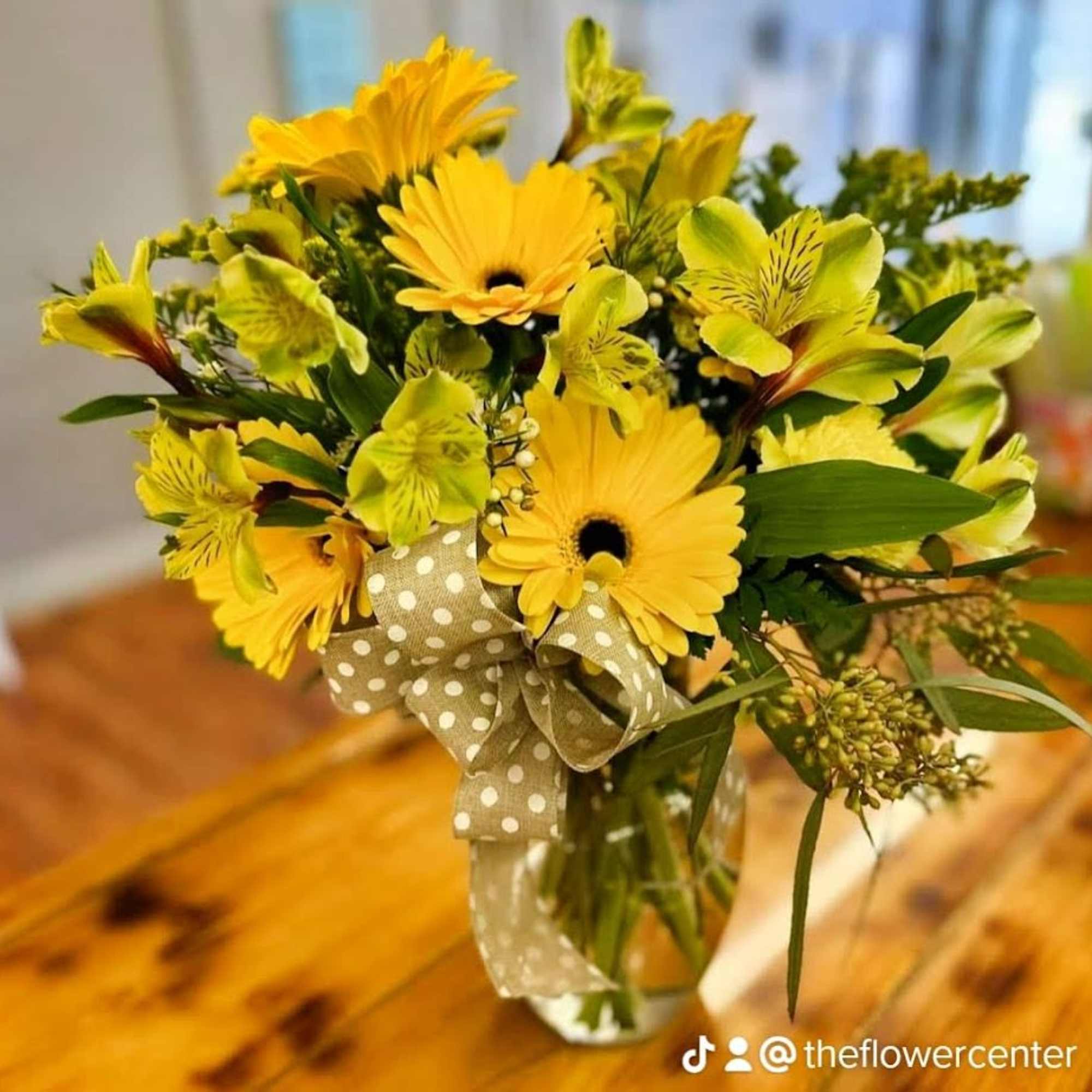 Yellow gerbera daisies and alstroemeria in a glass vase with a polka-dot ribbon