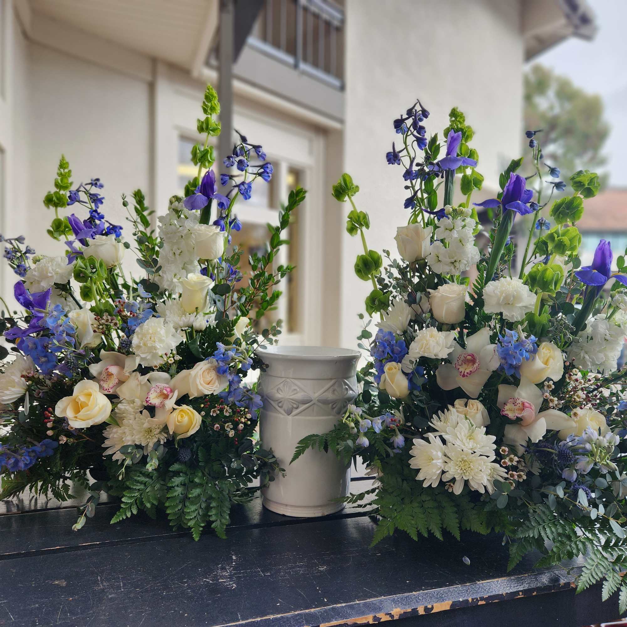 Two tall floral arrangements with white, blue, and purple flowers in white urns