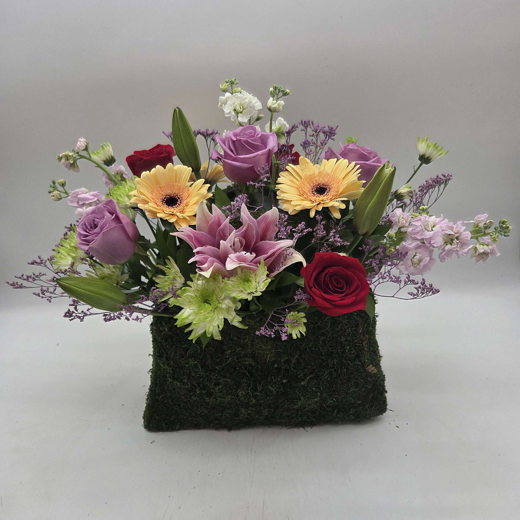 Charming floral arrangement designed in a moss-covered purse container, filled with fresh