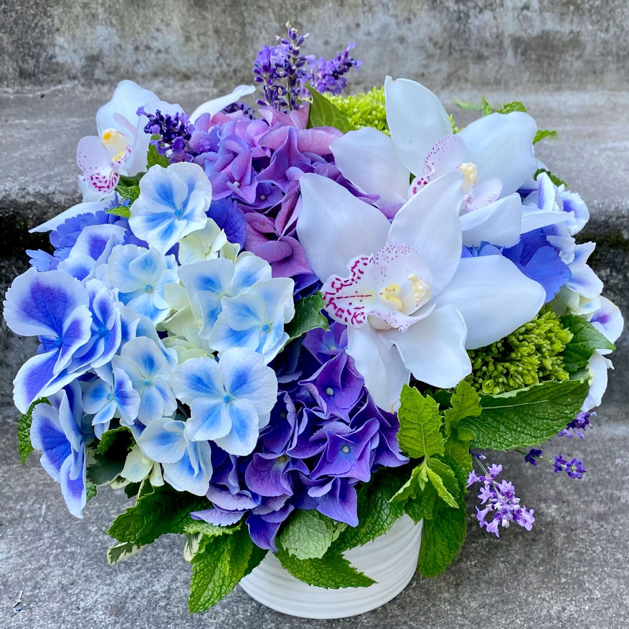 Blue and purple floral arrangement in a white vase with white orchids