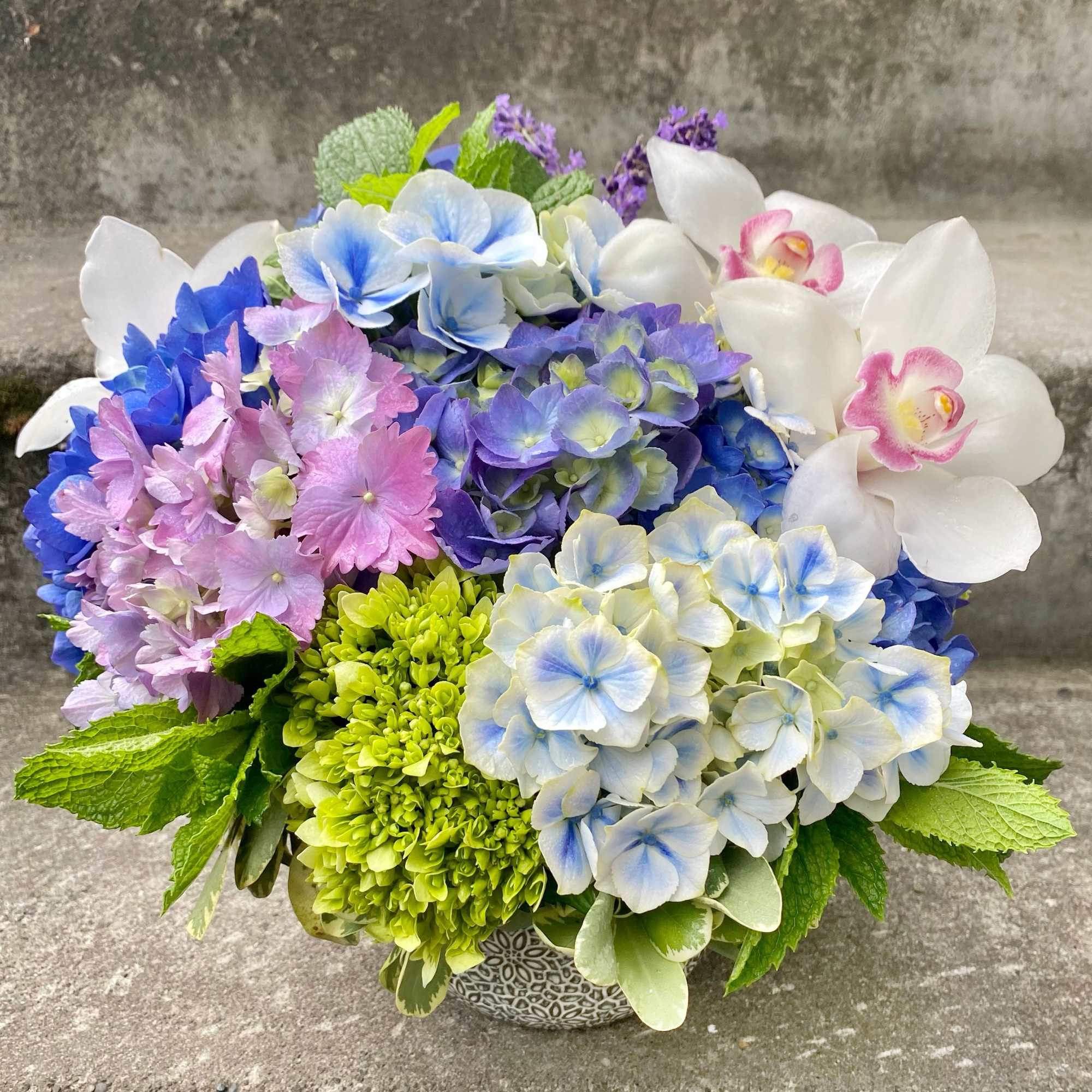 Colorful hydrangea and orchid arrangement in a patterned bowl