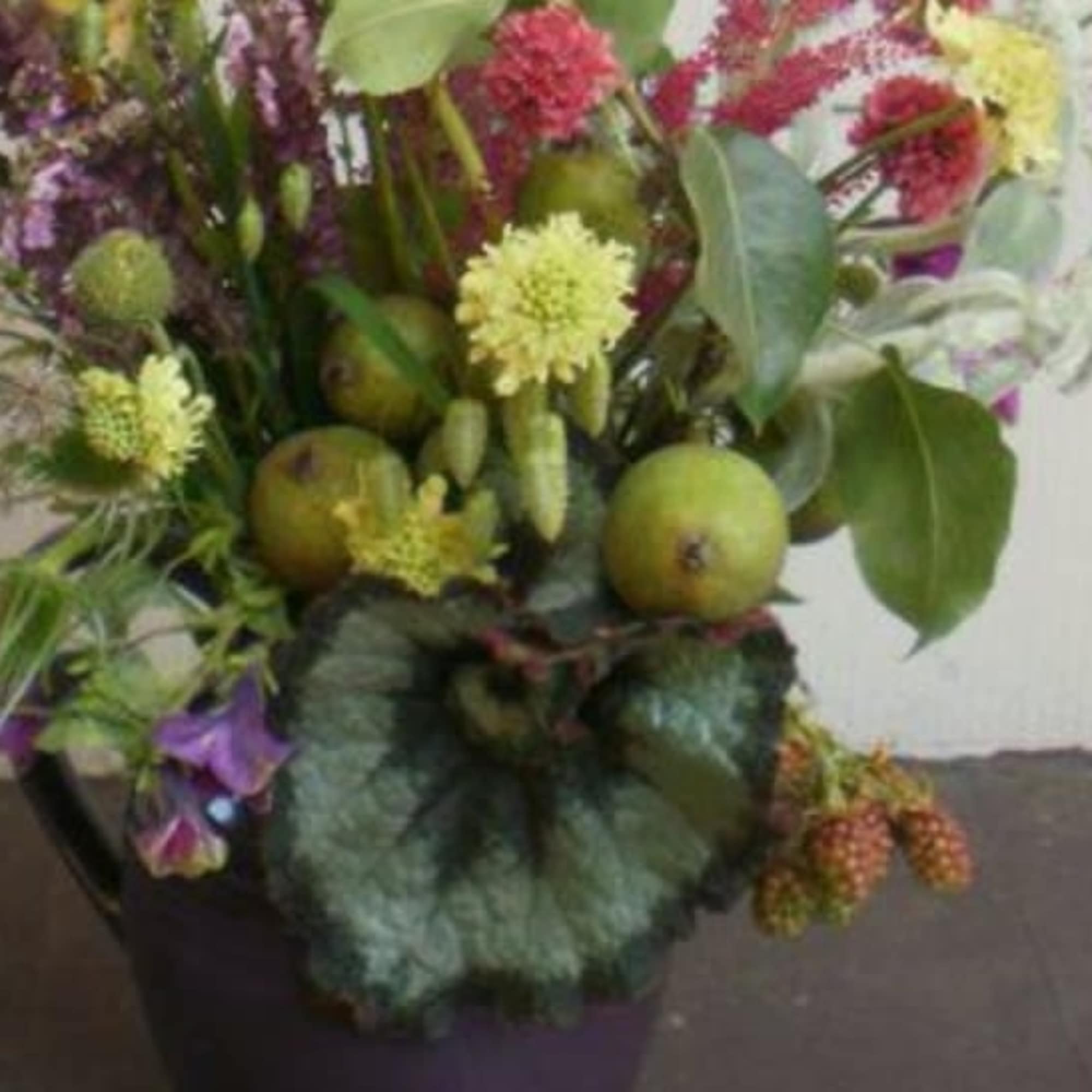 Rustic mixed arrangement with yellow flowers, green fruit, and berries in a dark metal bucket