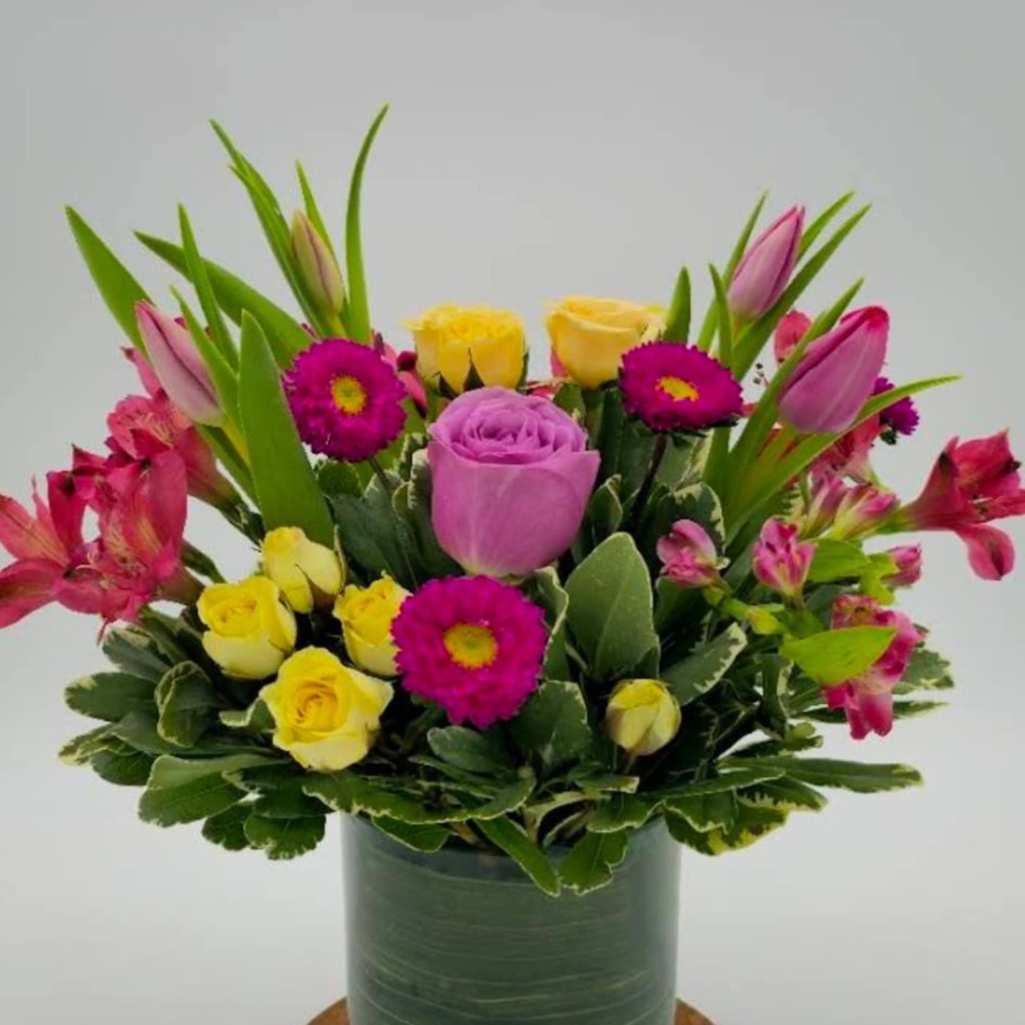 Mixed bouquet of pink, yellow, and purple flowers in a glass vase