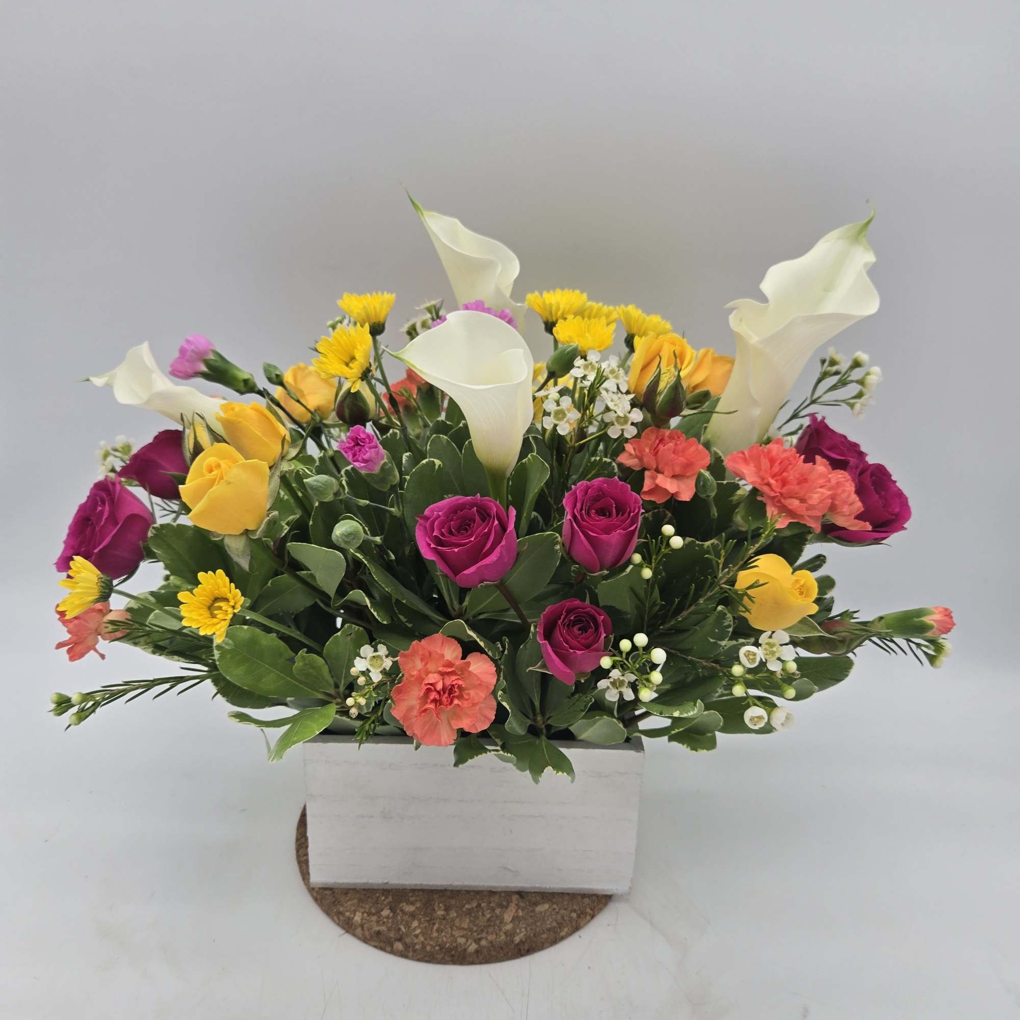 Mixed bouquet with pink roses, yellow blooms, white calla lilies, and carnations in a white box