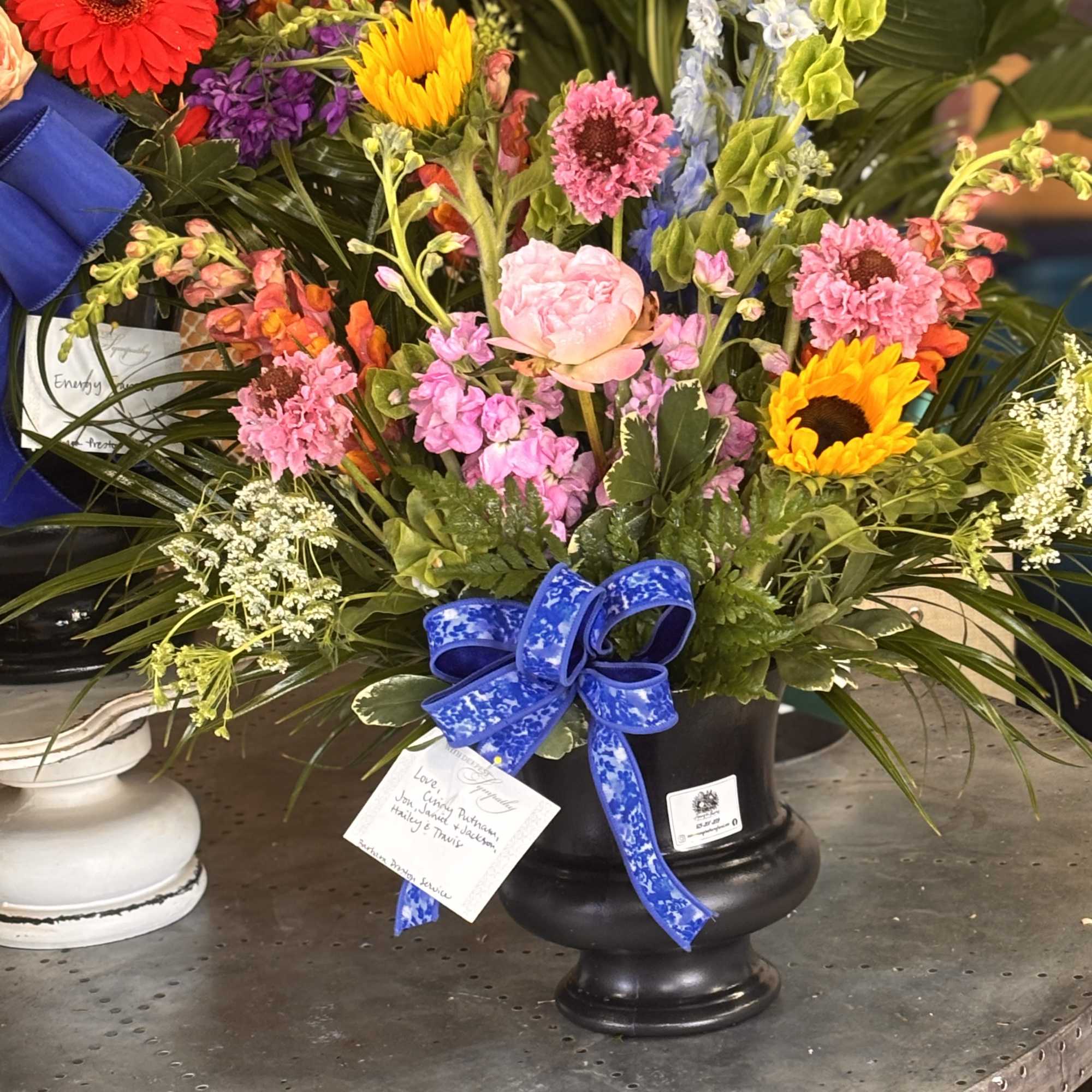 Bright, uplifted blooms in a black urn create a comforting yet celebratory